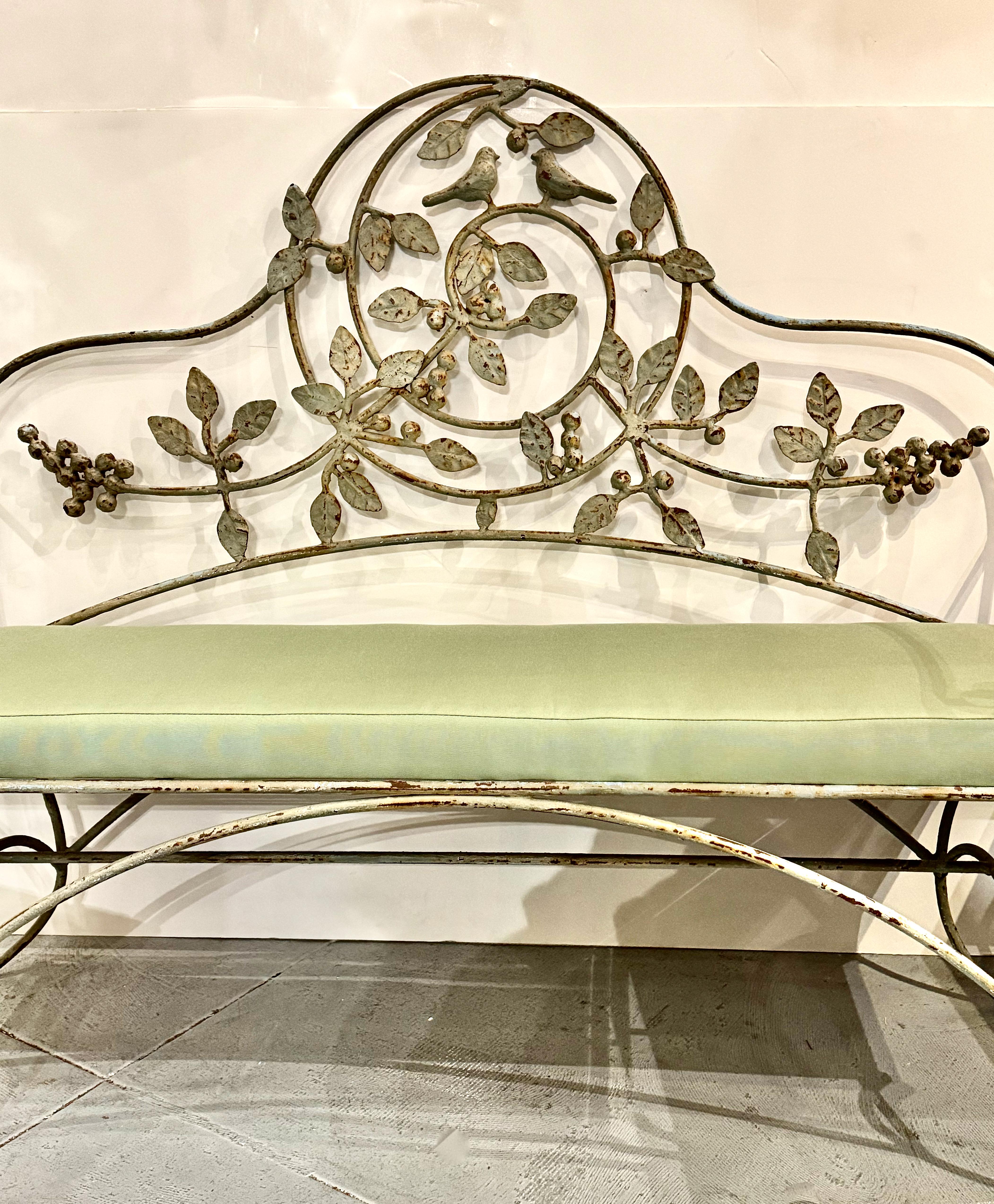 This is a sweet forged iron garden bench that is beautifully accentuated with iron leaves, grapes and love birds. The bench is in very good original condition and is highlighted by a new cushion. Although the bench was a designed for out door use,