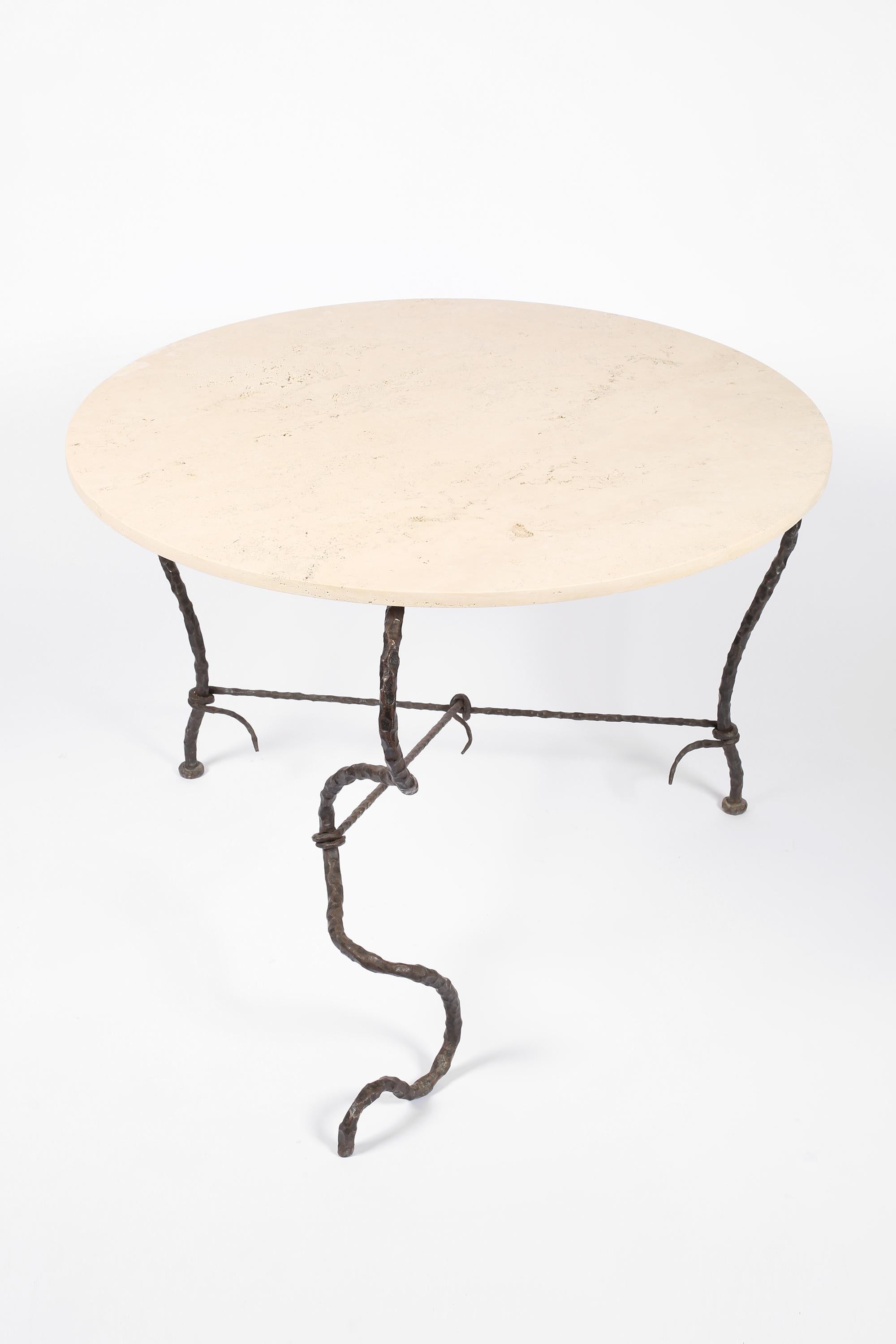 A statement, surrealist centre or dining table in forged iron with a circular travertine limestone top. The organic, serpent-like base bound by coiled supports in the manner of Diego Giacometti. French, c. 1950s.