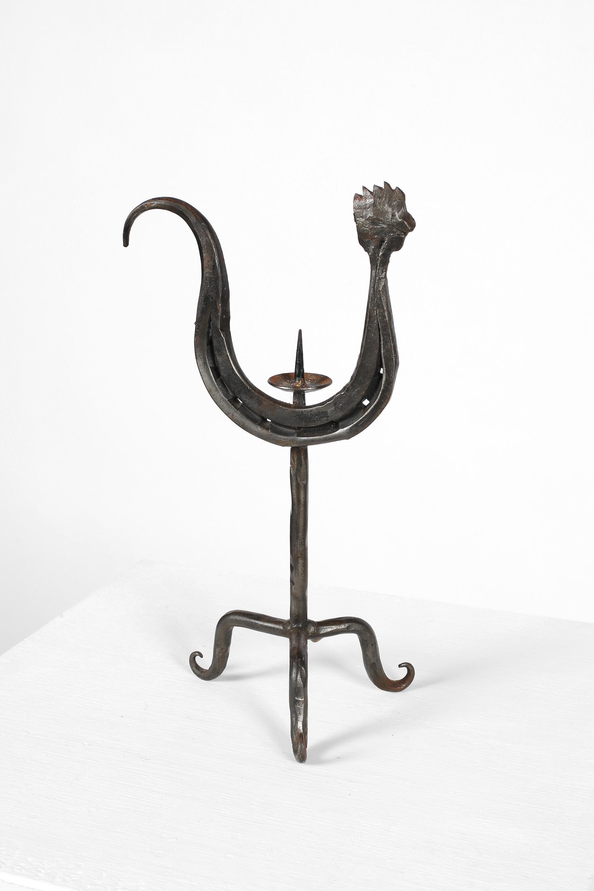 A hand forged zoomorphic iron candlestick stylised as a cockerel on a three point base. In the manner of work by Jean Touret and Les Artisans de Marolles. French, c. 1950s. 