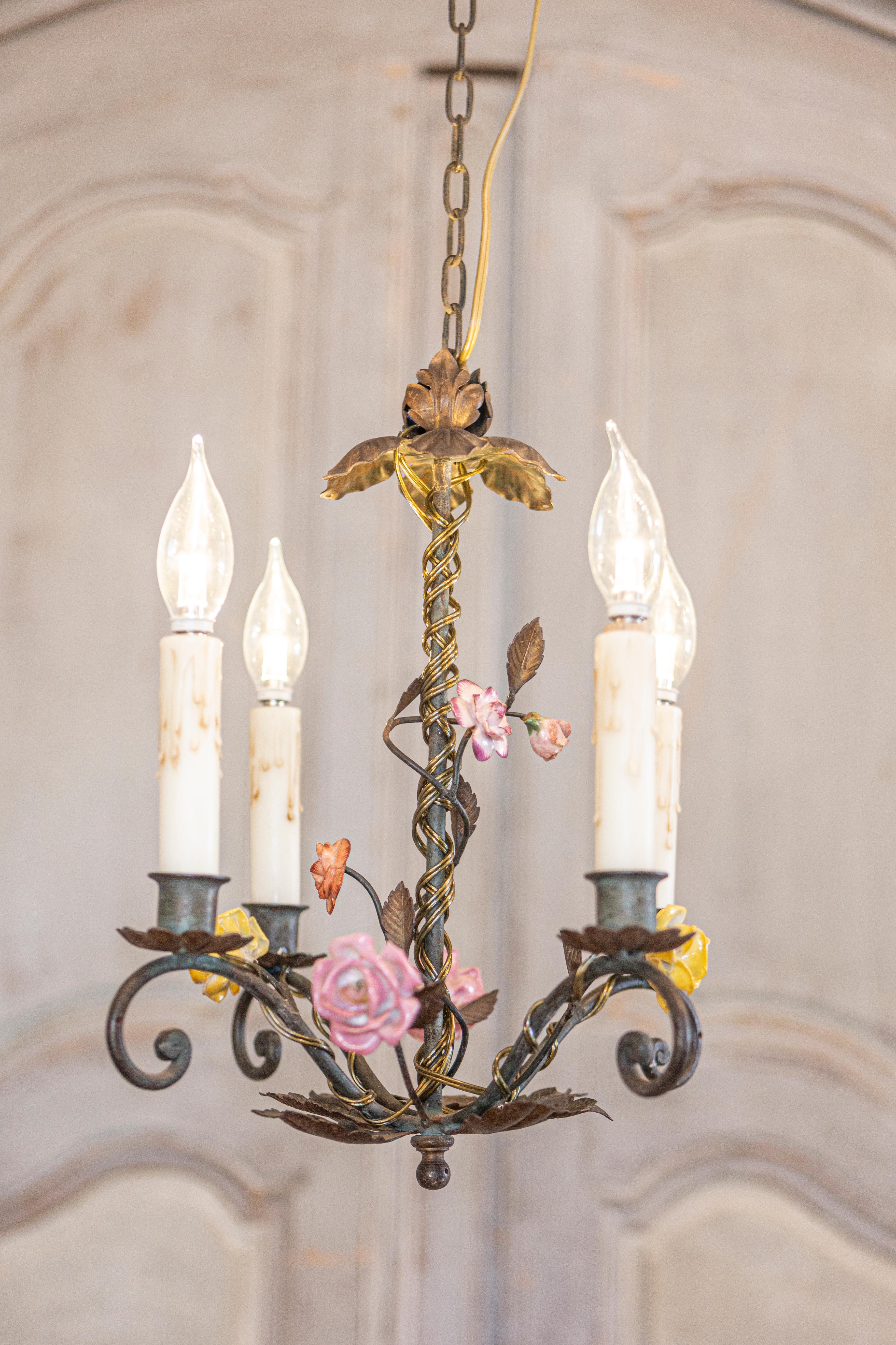 A French iron or tôle four-light chandelier from the 20th century with hand-painted porcelain roses, scrolling arms and foliage, professionally rewired for the USA. This enchanting French four-light chandelier from the 20th century blends the rustic