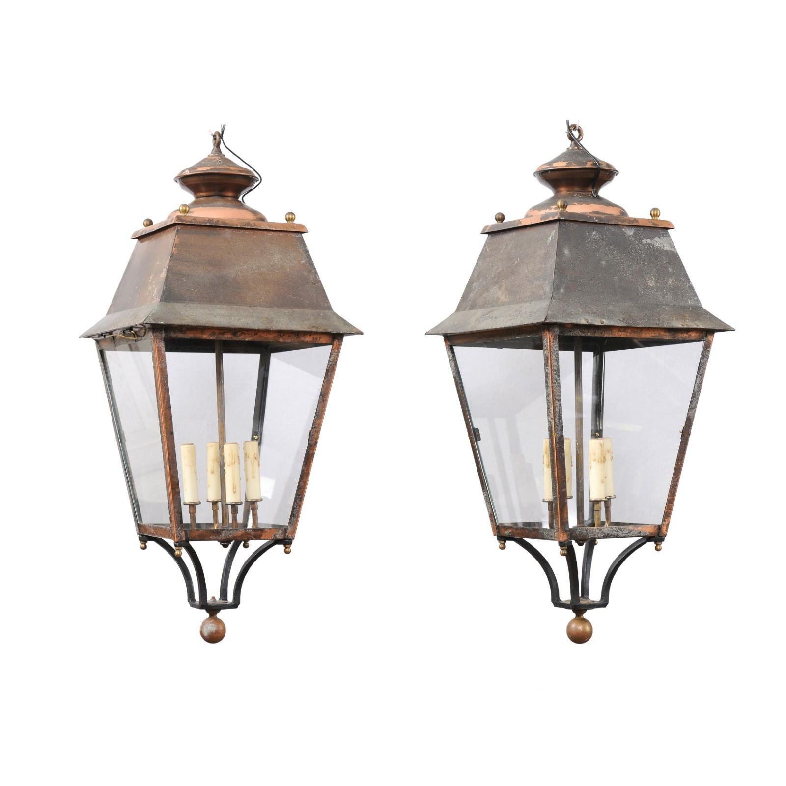 Two French copper lanterns from the 20th century, with four lights, glass panels, petite finial and rustic character. This pair of French copper lanterns, crafted in the 20th century, exudes a timeless allure with their rustic character and