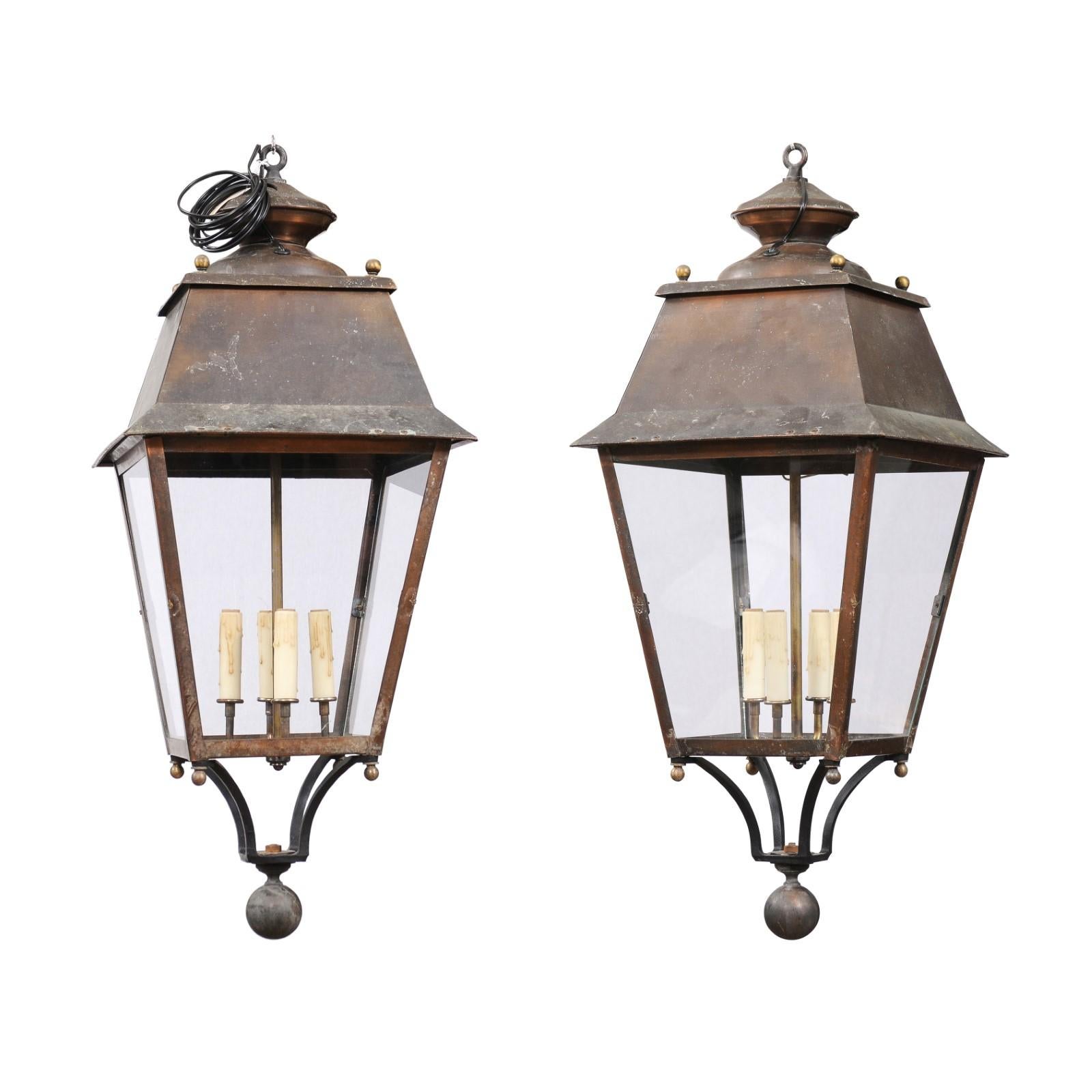 Two French copper lanterns from the 20th century, with four lights, glass panels, petite finial and rustic character. Elevate your home's ambiance with these elegant French copper lanterns, dating back to the 20th century, each featuring a quartet