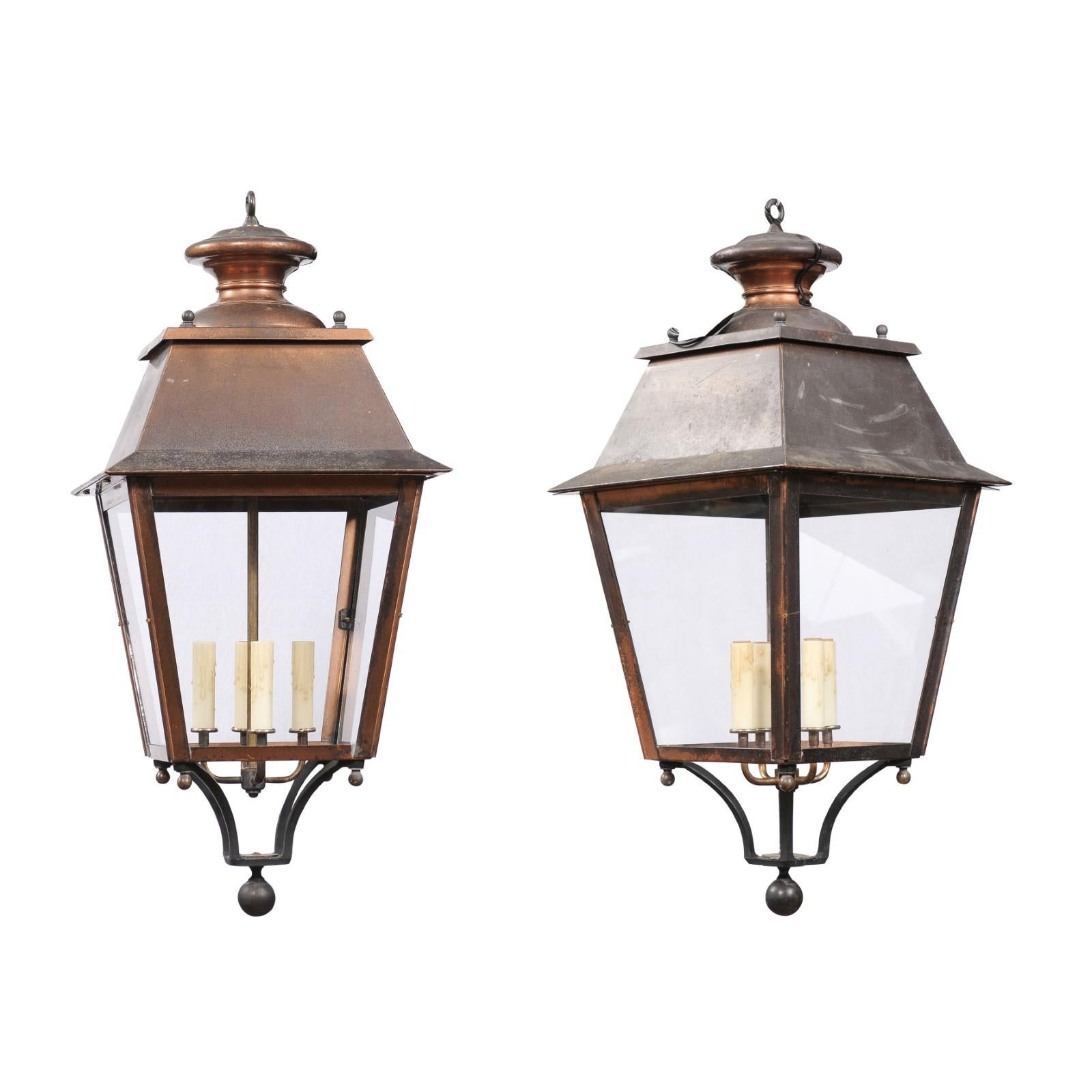 Two French copper lanterns from the 20th century, with four lights, glass panels, petite finial and rustic character. Emanating a warm, rustic charm, these two French copper lanterns from the 20th century are a quintessential blend of classic design
