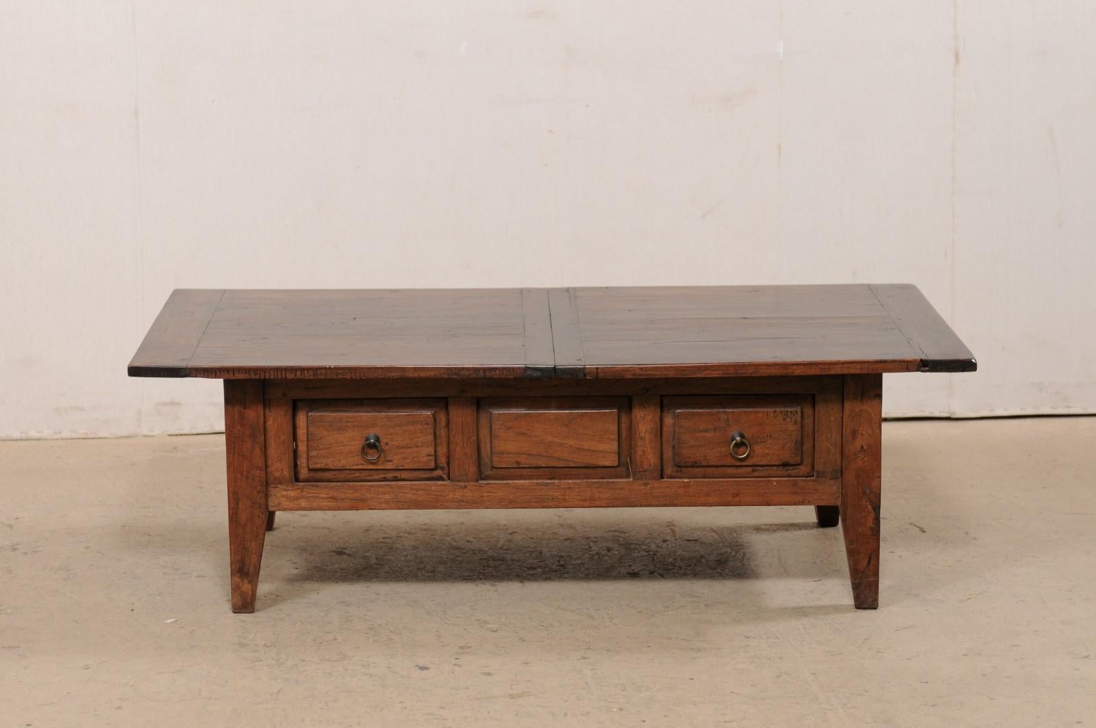 A French coffee table with two drawers from the early 20th century. This antique coffee table has a rectangular-shaped top which hangs over an apron below that houses a pair of raised-panel front drawers at one long side, with the raised panel motif