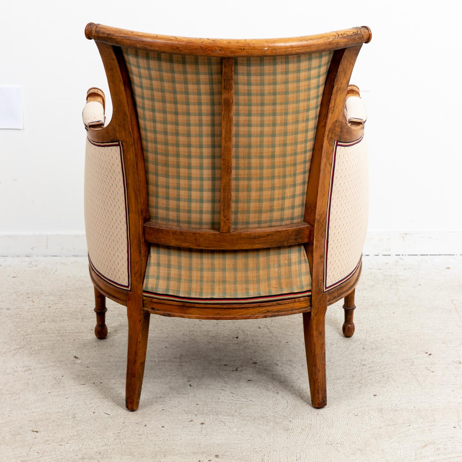 Circa late 19th century French fruitwood Louis XVI Empire Directoire style bergère chair upholstered in a white fabric with trim and a contrasting check fabric on the back. The chair also features vase-and-ring turned arm supports and ring turned