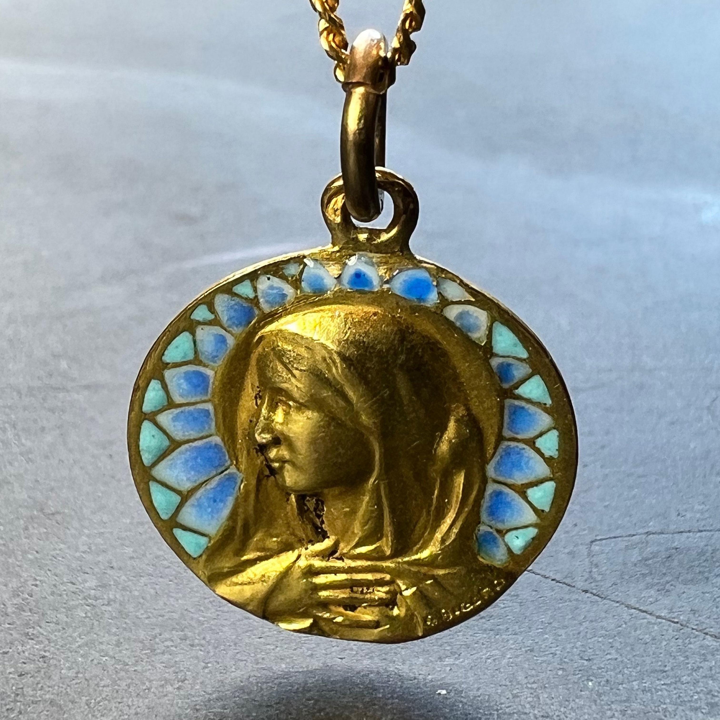 A French 18 karat (18K) yellow gold charm pendant designed as a round medal depicting the Virgin Mary with plique a jour turquoise and blue graduated enamel surround. Signed G Bigard, stamped with the eagle’s head for 18 karat gold and French