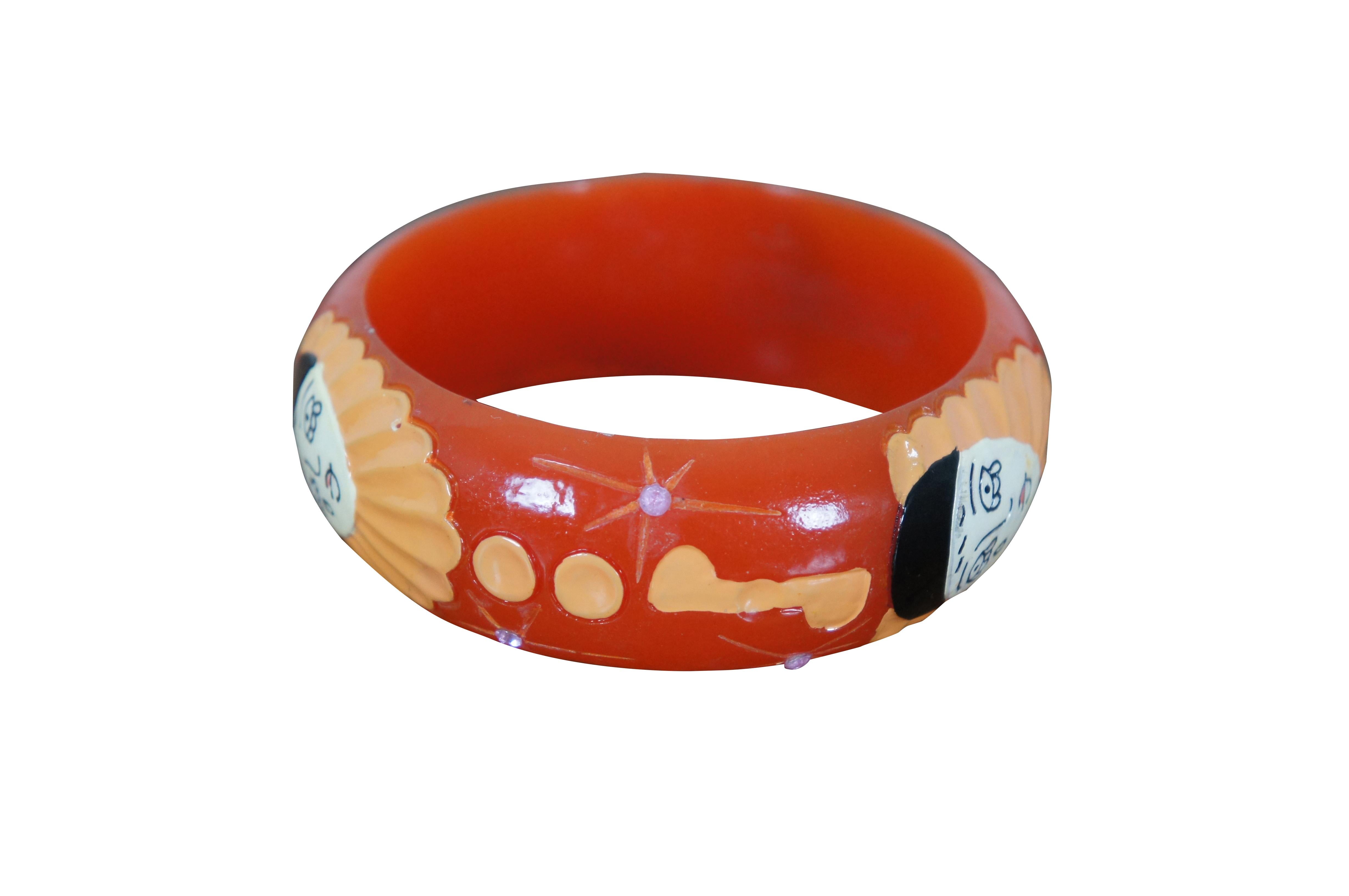 Vintage pumpkin orange Bakelite bangle bracelet featuring a carved and painted Pierrot (ala Commedia del Arte) faces, dots, and music notes, with a smattering to stars studded with white rhinestones. Butler & Wilson Galalith bangle design, inspired