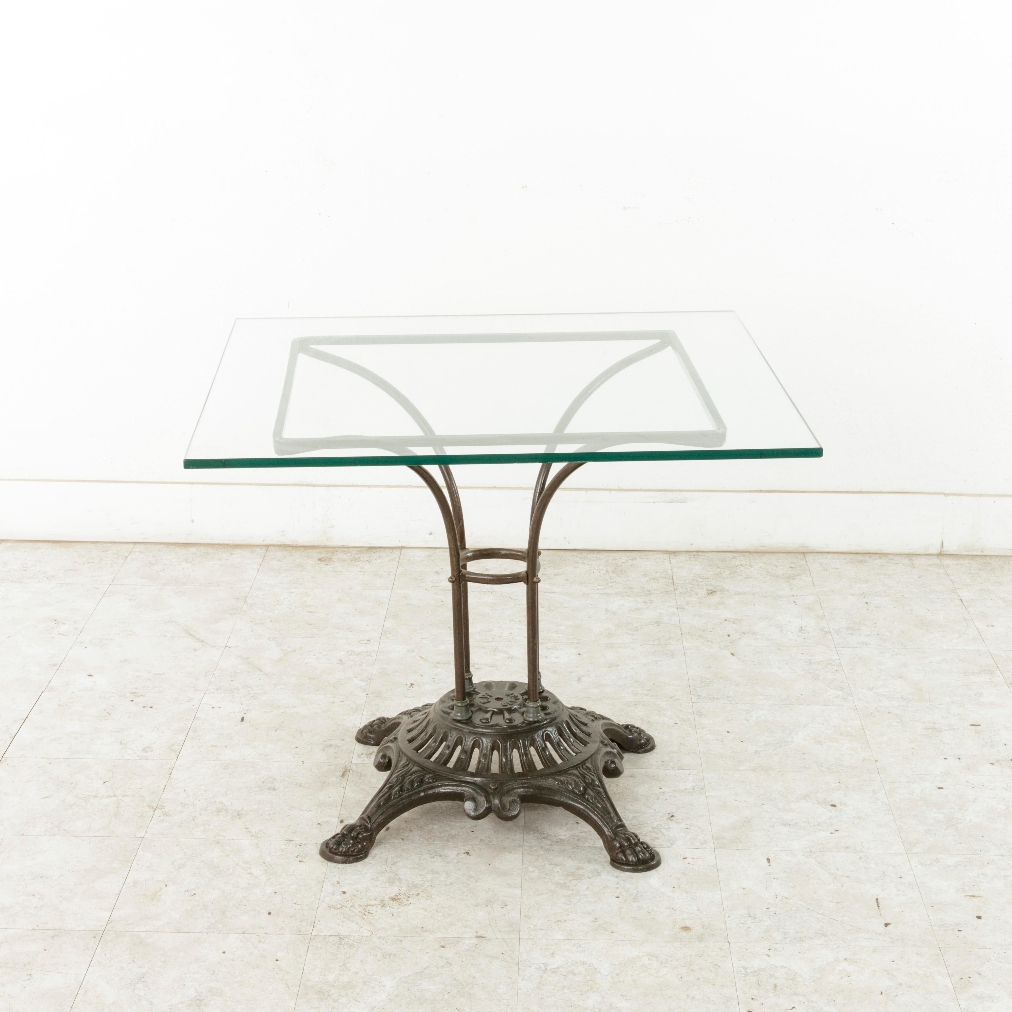 This French garden table from the turn of the twentieth century features a pierced cast iron base detailed with scrolling and claw feet. The base is marked F.W. Depose (trademarked). Four iron rods join the base to the square iron support that holds