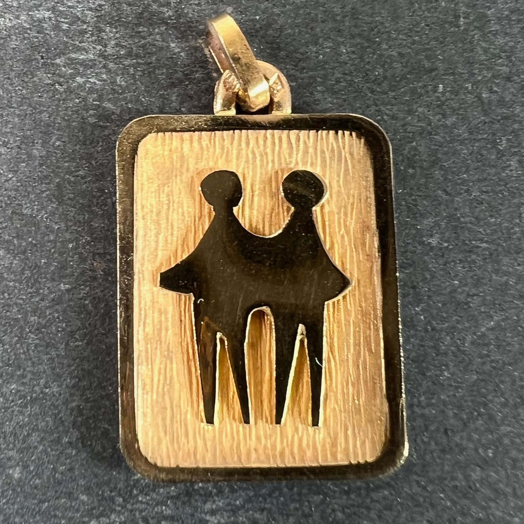 A French 18 karat (18K) yellow gold charm pendant designed as a rectangular medal with an engraved recess depicting a pair of people representing the zodiac star sign of Gemini. Stamped with the eagle’s head for French manufacture and 18 karat gold