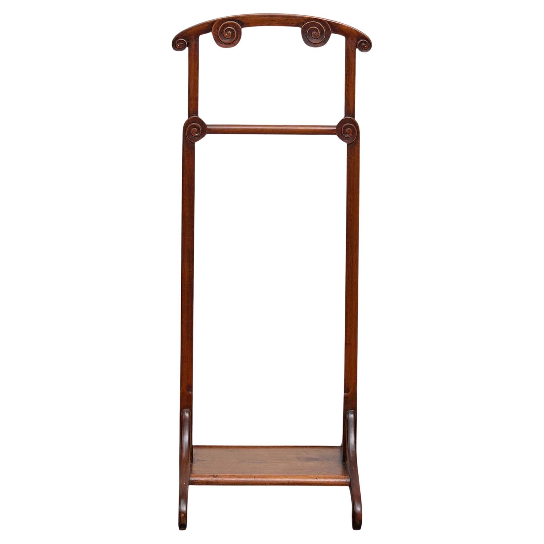 Valet de chambre français en bois aux tons chauds, datant probablement du début du XXe siècle, conçu avec d'élégants accents de volutes au niveau de la crête, des articulations et des pieds. Grand et fin, il est à la fois pratique et élégant. Il
