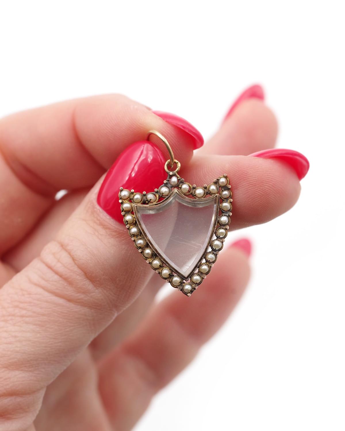 Georgian shield locket pendant in 18 karat yellow gold. This coat of arms medallion opens with a hinged glass back, allowing you to slip a sentimental item into it. The entire frame is adorned with small, fine pearls. The First Empire pendant, circa