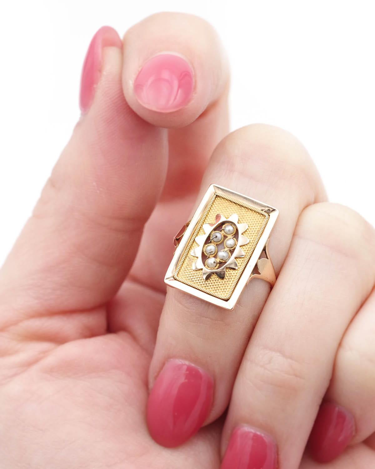 French Georgian pearl ring in 18 karat gold, rectangular in shape and centered with 6 fine pearls held by gold threads in an oval star decoration, on a background of small matte gold dots. The band is thin and the shoulders of the ring are decorated