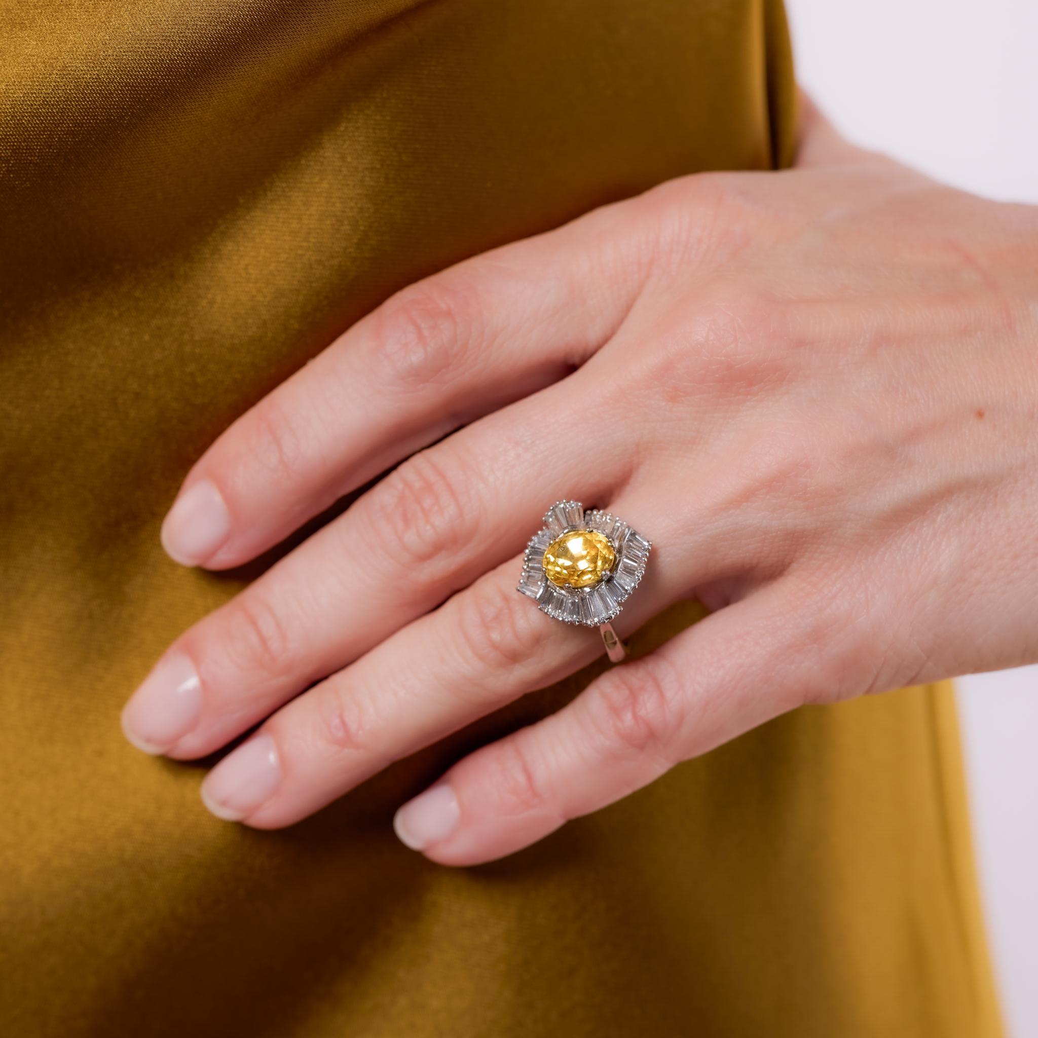 Crafted in the 1960s, this French Mid Century ballerina ring showcases a GIA-certified 3.65-carat oval cut yellow sapphire from Ceylon, enhanced with heat treatment to reveal its golden hue. Surrounded by 26 baguette cut diamonds totaling