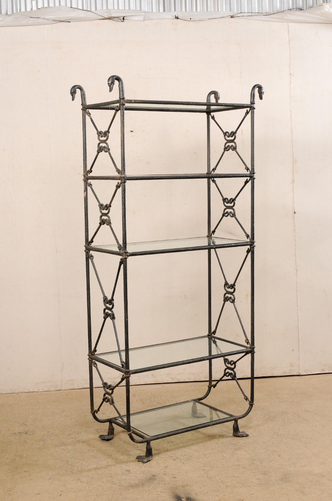 A French Giacometti style open display metal étagère with glass shelves. This vintage book shelf from France has a whimsical design which is reminiscent of Giacometti style. The patinated iron frame is topped with goose-head finials at each corner,