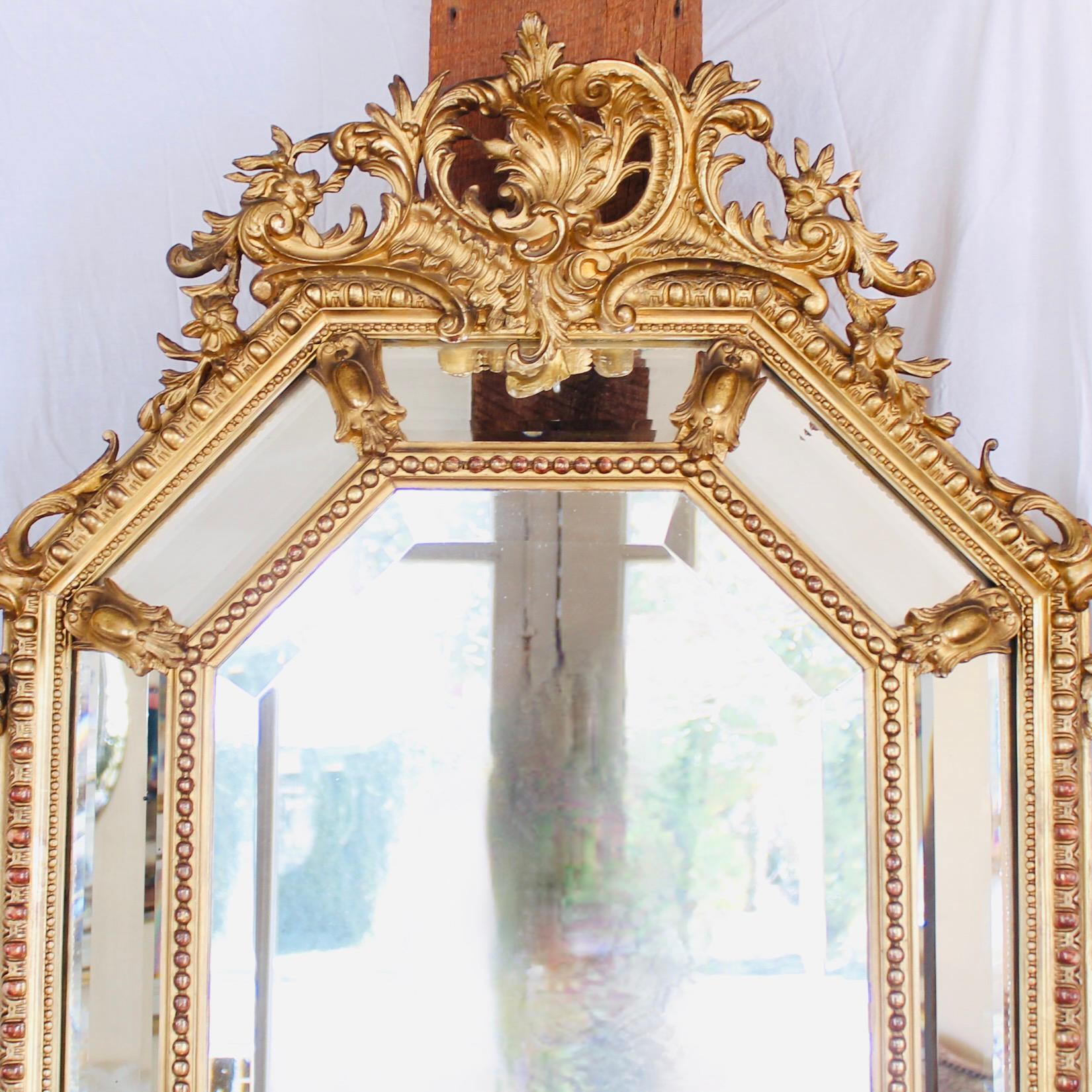 An eye-catching confection of Rococo decorative elements, combined in a cushion mirror with sober classical architectural moldings: egg and dart with pearl edging arranged in an octagonal format around a central mirror plate. The crest is