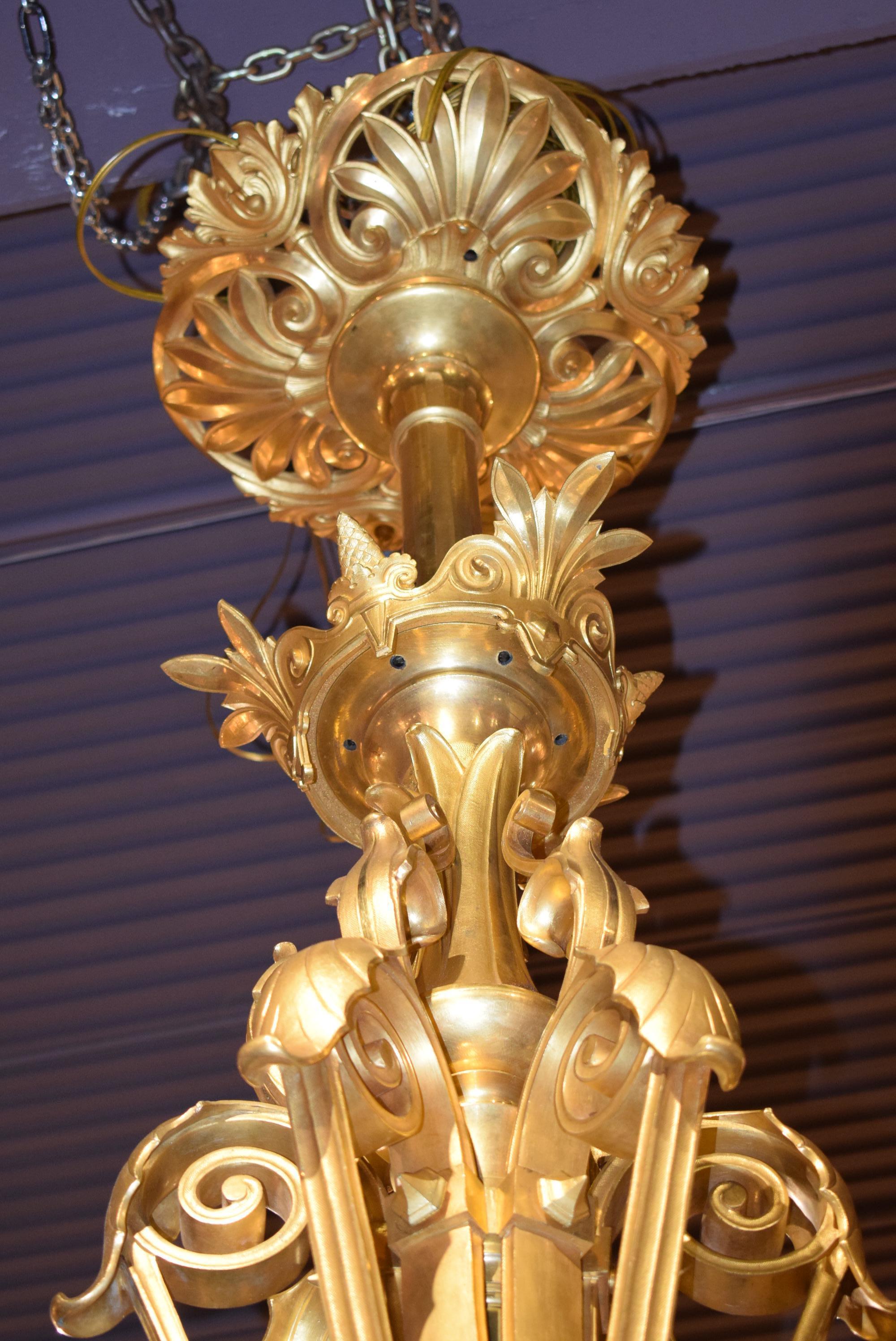 Très important lustre en bronze doré, à six bras de lumières, volutes et feuillages, supportant chacun trois lampes à huile ornées de coupelles en cristal sculpté en pointe de diamant. Décorations de feuillages. Monté sur l'électricité. Travail