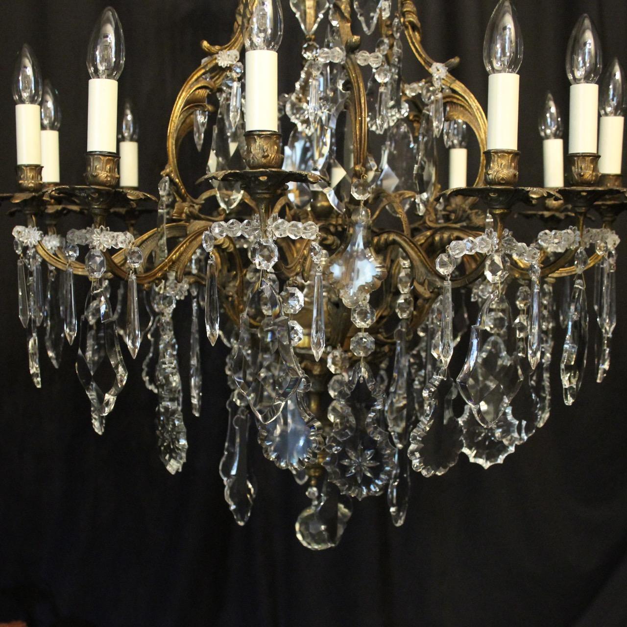 A French dark gilded bronze and crystal 12 light birdcage form antique chandelier, the leaf clad reeded scrolling arms with ornate bobeche drip pans and leaf bulbous candle sconces, issuing from an foliated cage form interior with a large prismatic
