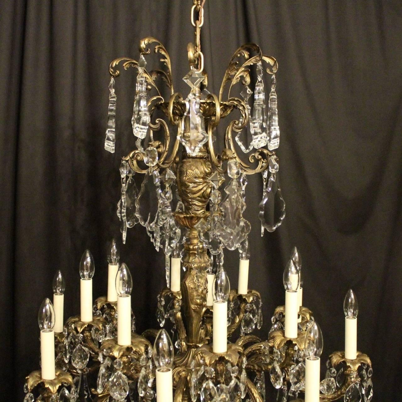 A large French gilded cast bronze and crystal sixteen-light double tiered antique chandelier, the eight and eight-light leaf scrolling arms with leaf bobeche drip pans, issuing from an ornate foliated baluster central column with a large scrolling