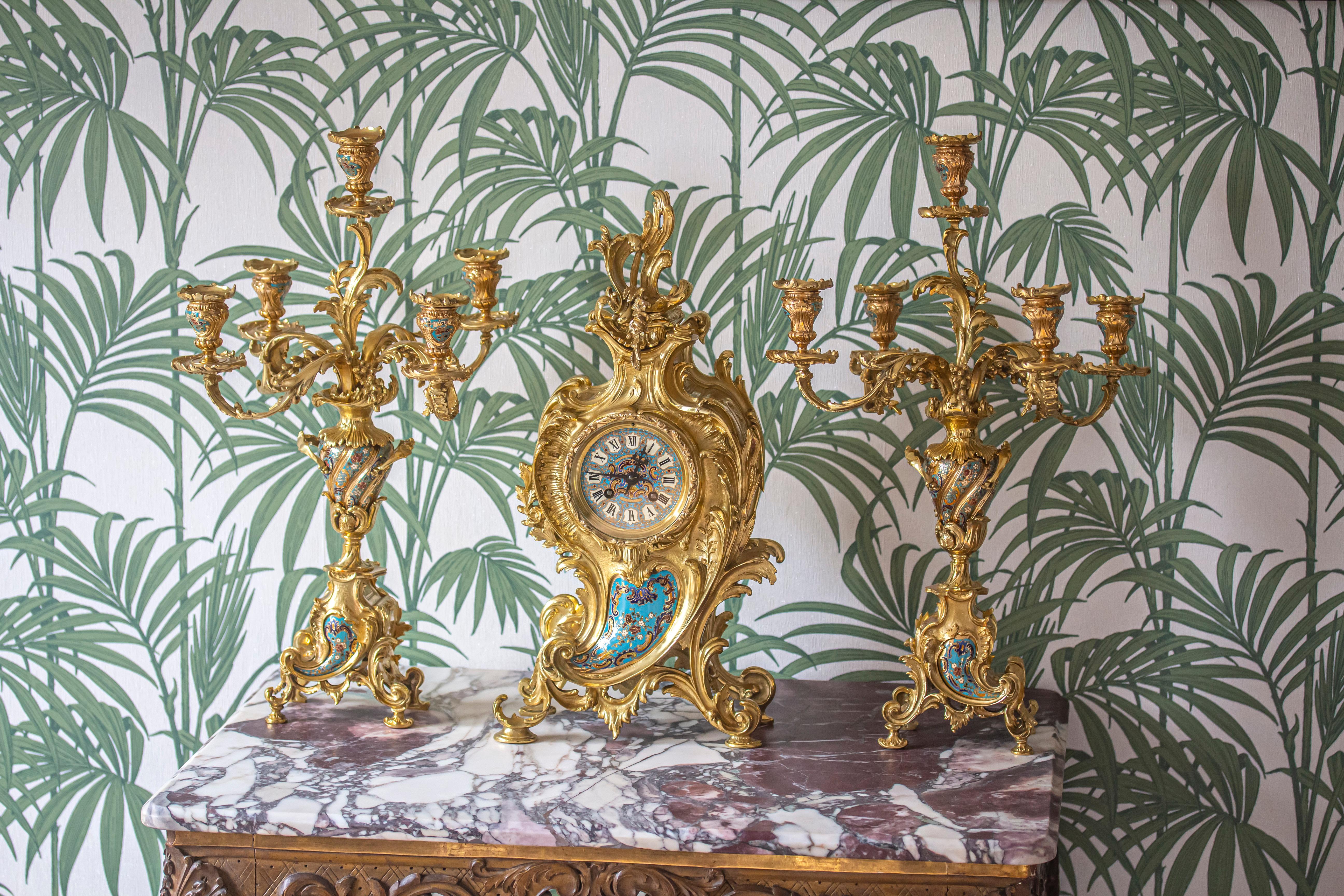 Fine French late 19th century three-piece clock garniture comprising of a pair of candle sticks and clock in a matching set. The garniture boldly cast with rococo influence in the Louis XV style decorated with a beautiful champlevé teardrop to the