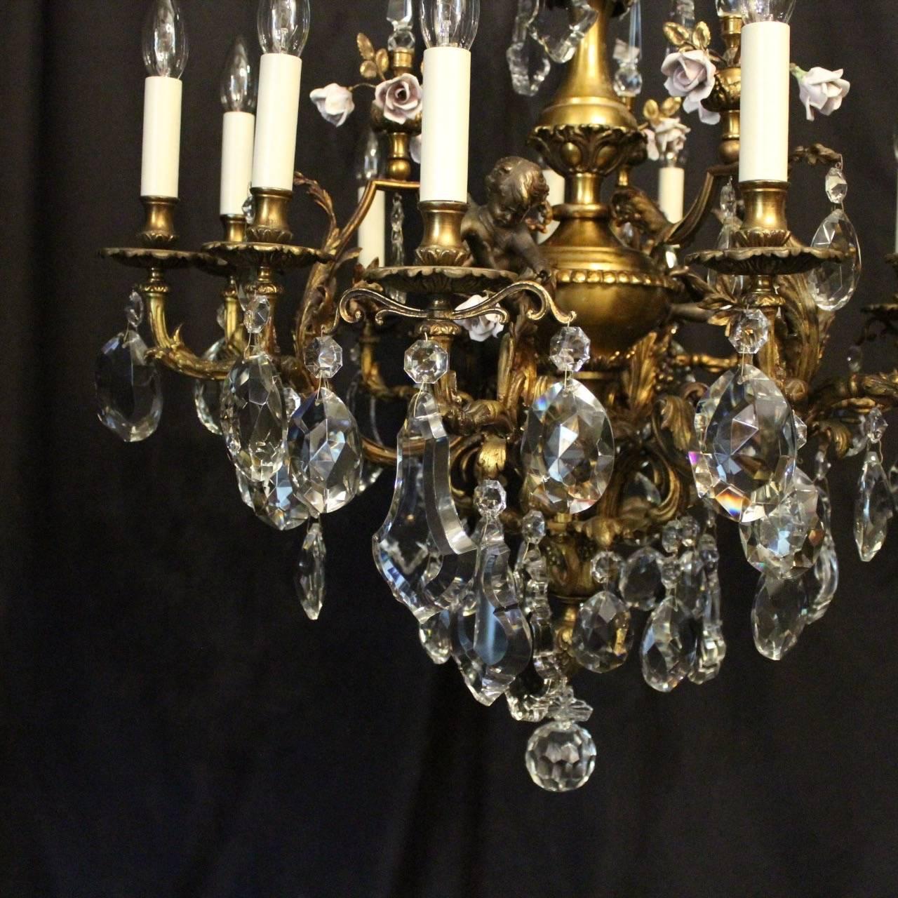 A French gilded bronze and crystal twelve-light cherub antique chandelier, the ornate acanthus leaf scrolling arms with circular bobeche drip pans and bulbous candle sconces, issuing from an foliated interior with ornate bronze cherubs and porcelain