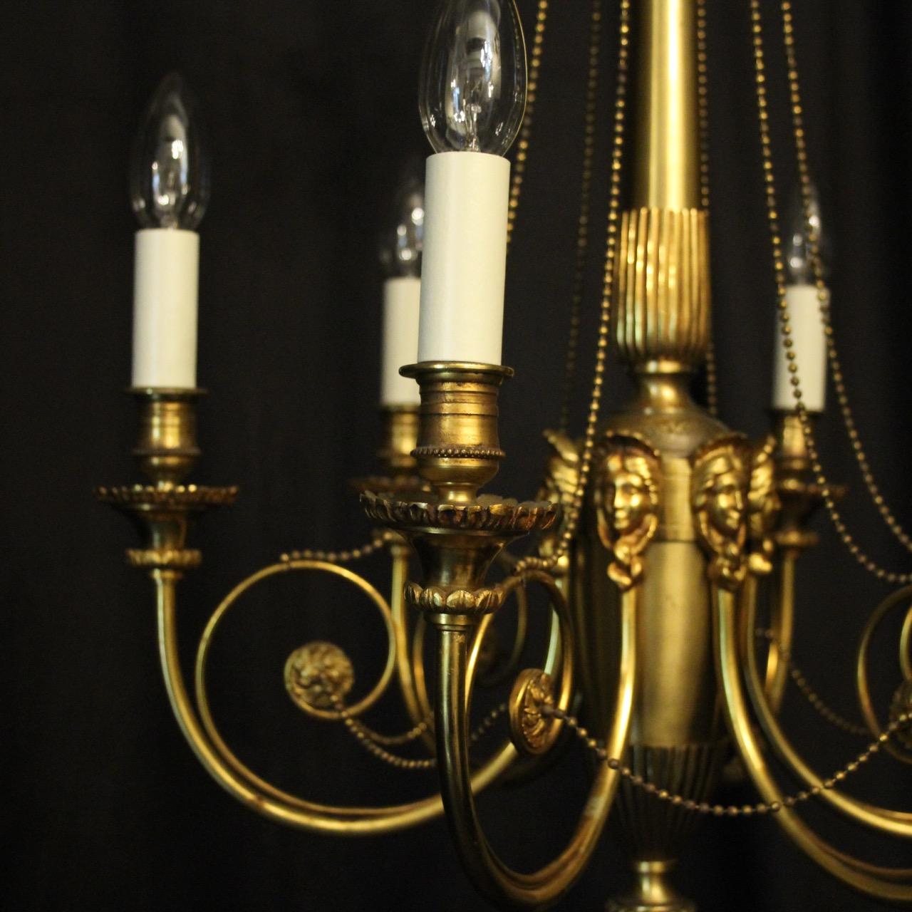 A French gilded brass 6-light antique chandelier, the scrolling arms with ornate trumpet bobeche drip pans and candle sconces, issuing from a tapering central column with six decorative female mask heads and reeded base, with interlinking gilded
