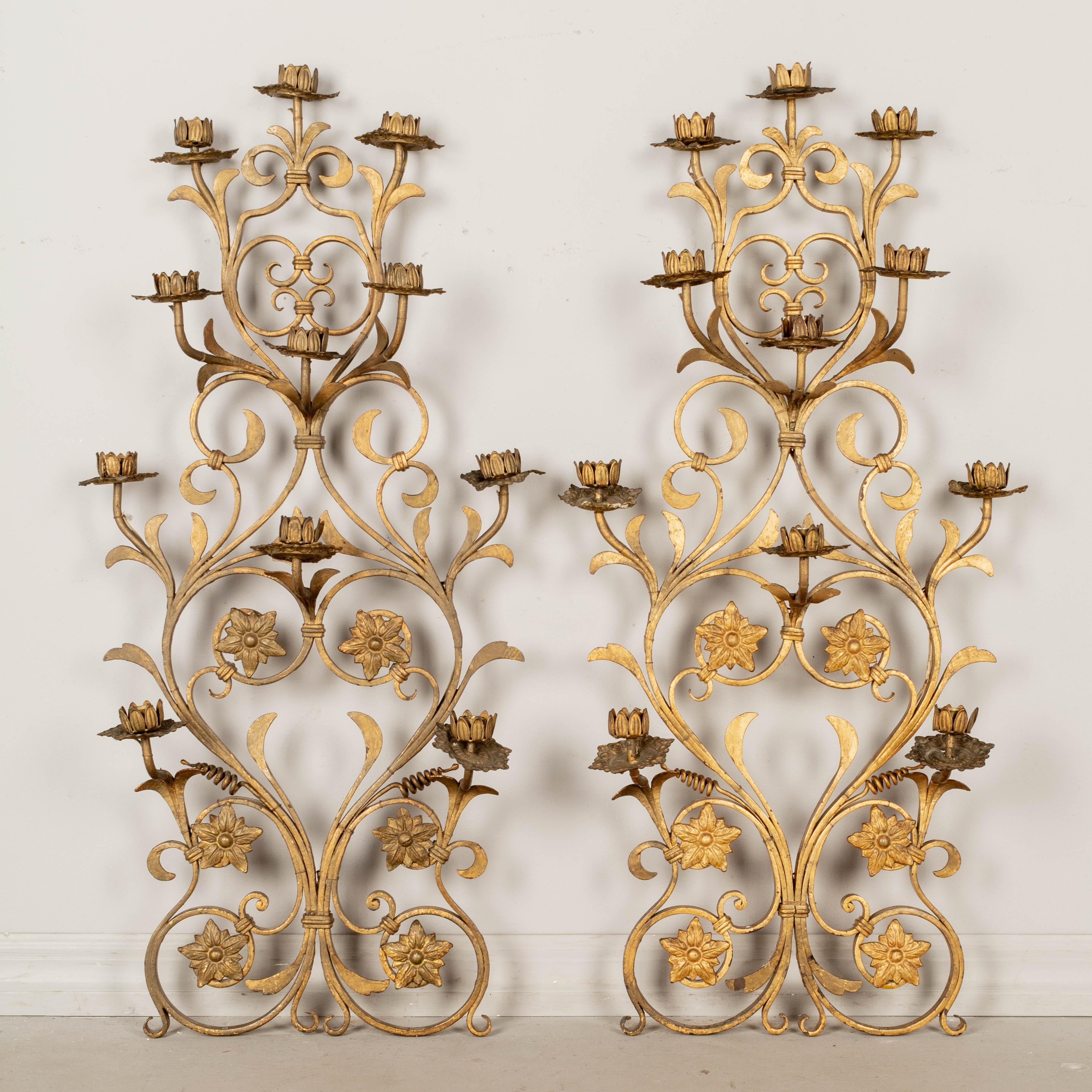 A pair of French gilt wrought iron and tôle eleven-light candelabra sconces decorated with cast iron rosettes. Nice iron work with stamped brass tôle candle cups and bobeches (some slightly bent). These were large floor candelabra and are missing