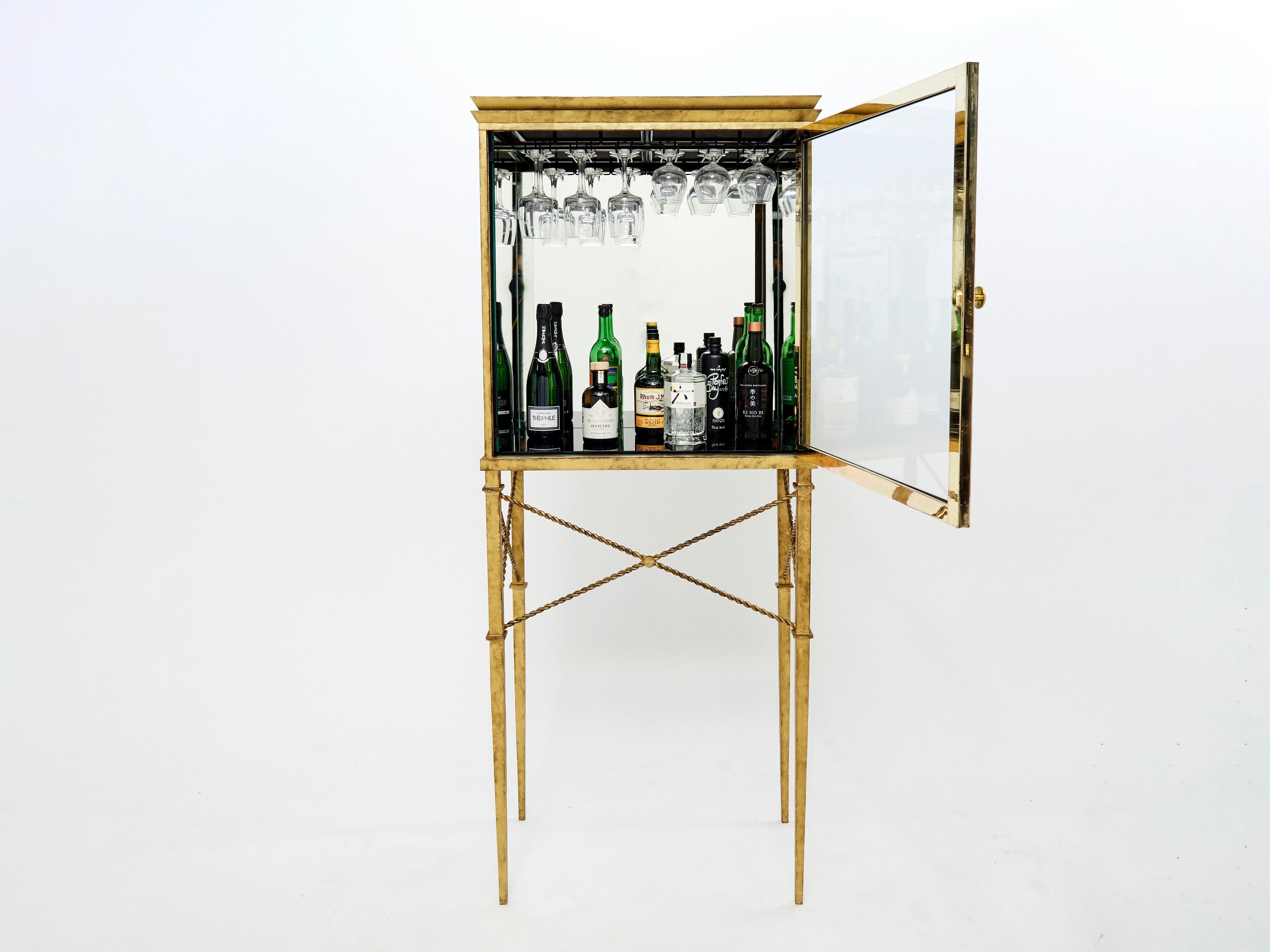 A unique French Art deco vitrine bar cabinet produced in the 1920s. The wrought iron feet are glittering in an antiqued gold gilt finish, with beautiful details, while the mirrored vitrine cabinet part gives the piece a glam twist. Its sophisticated