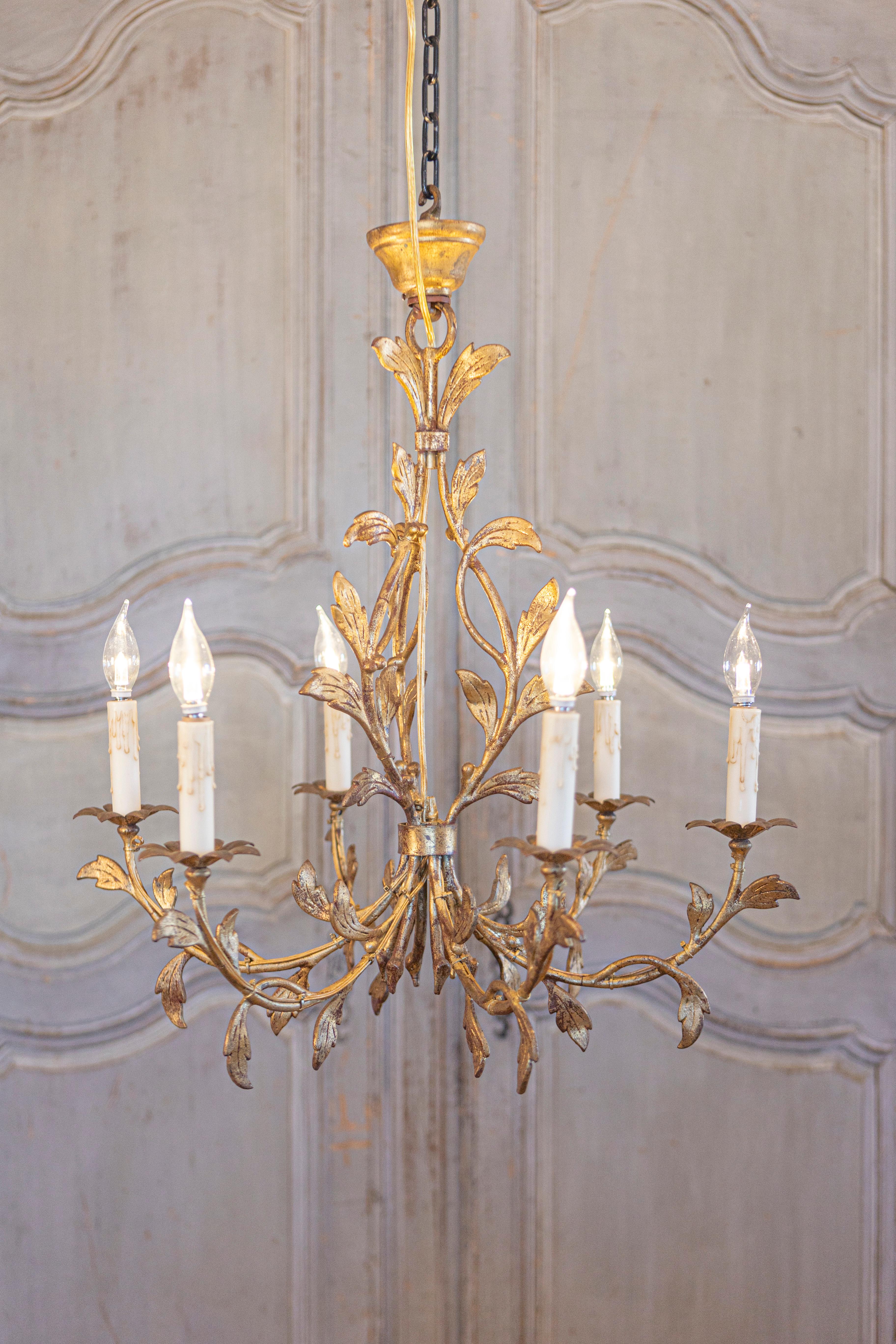 A French gilded iron six-light chandelier with foliage motifs. This French gilded iron chandelier, a treasure from the 20th century, enchants with its six lights and a symphony of foliage motifs that dance across its structure. The chandelier's
