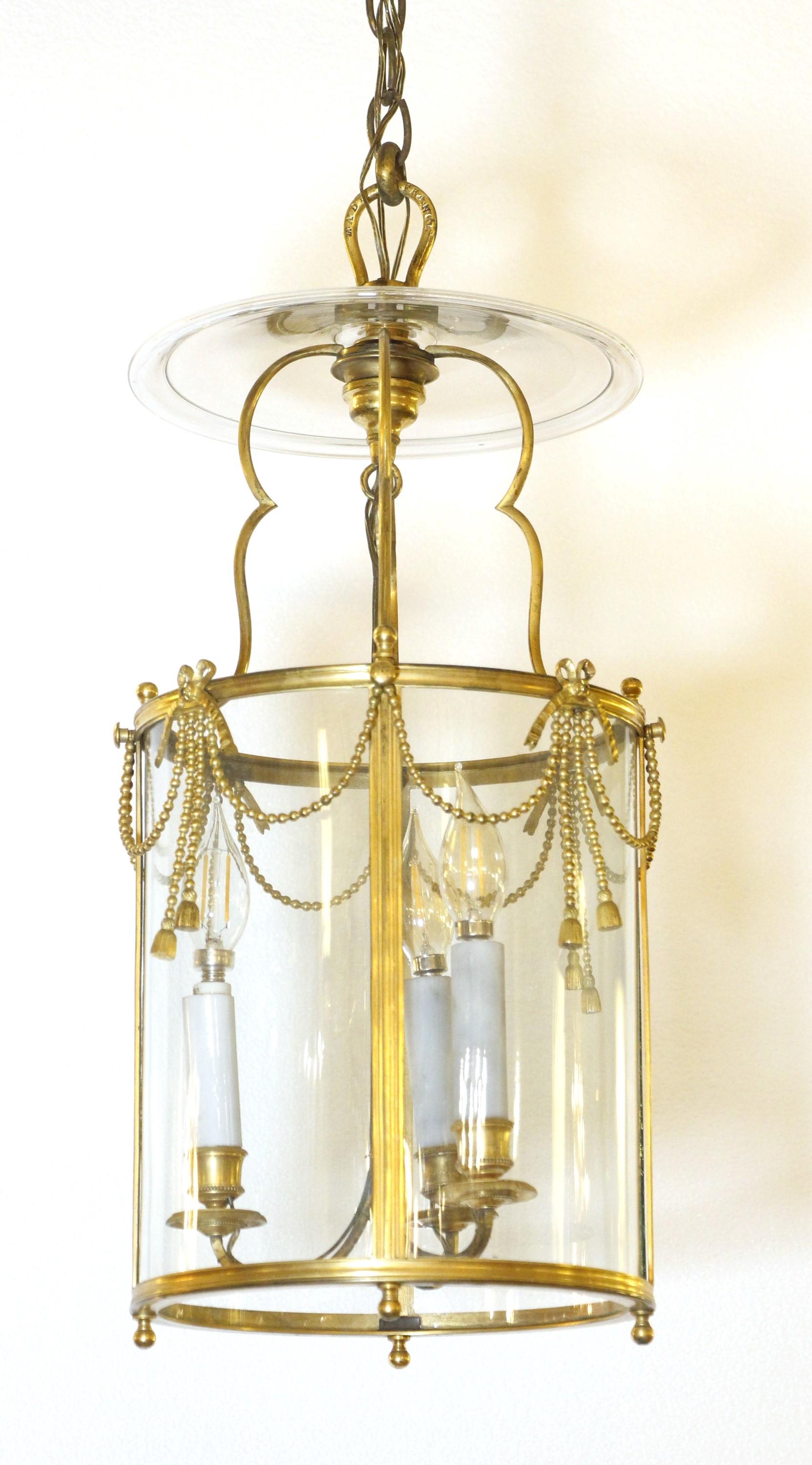 Bronze gold gilded, three light, 20th C., lantern light with canopy. It is adorned with a series of chain swags with molded tassels and ribbons decorating the cylinder glass. The bottom features four small finials. This is wired and ready to ship.