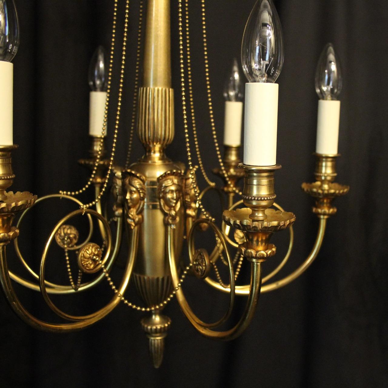 A French pair of gilded brass Lucien Gau 6-light antique chandeliers, the scrolling arms with ornate trumpet bobeche drip pans and candle sconces, issuing from a tapering central column with six decorative female mask heads and reeded base, with