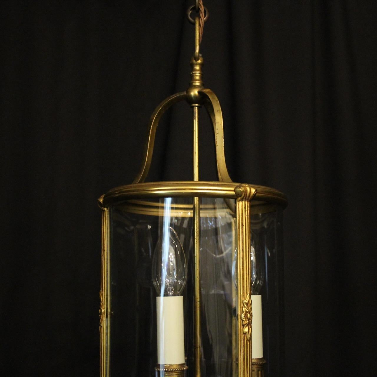 A French gilded cast brass triple light antique hall lantern, the three scrolling light fittings with circular bobeche drip pans and reeded candle sconces, surrounded by a sectional circular convex glass panels and held within a decorative scrolling