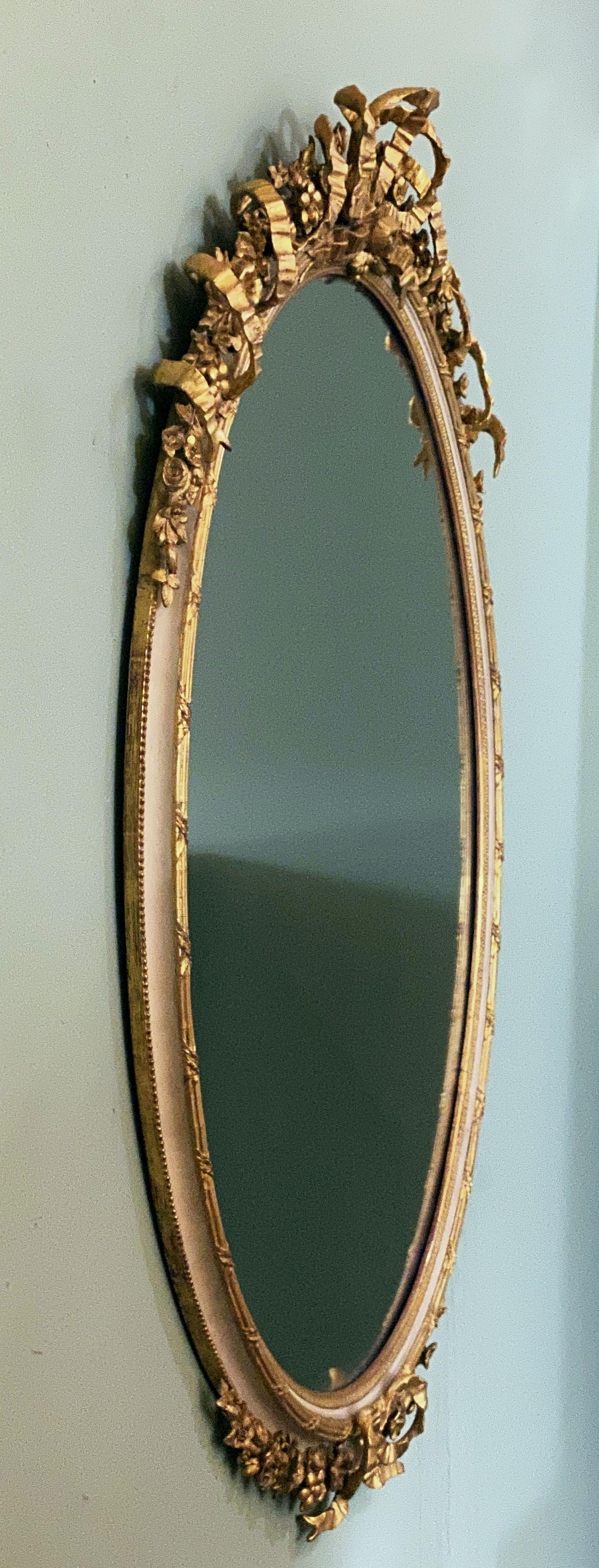 A fine French gilt and parcel cream painted oval wall or hall mirror with ribbon tied floral crest and lower frieze - in the Louis XVI manner with rococo or baroque styling.

Dimensions are: Height 57 inches x Width 42 1/2 inches x Depth 5 inches
