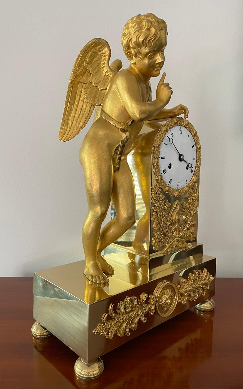 A beautiful early French Cherub mantel clock, circa 1830 with gilt brass case, the ceramic dial is in excellent condition with no chips or cracks, with breguet hands, the bezel is decorated with flowers above a pair of foliate swags with a standing