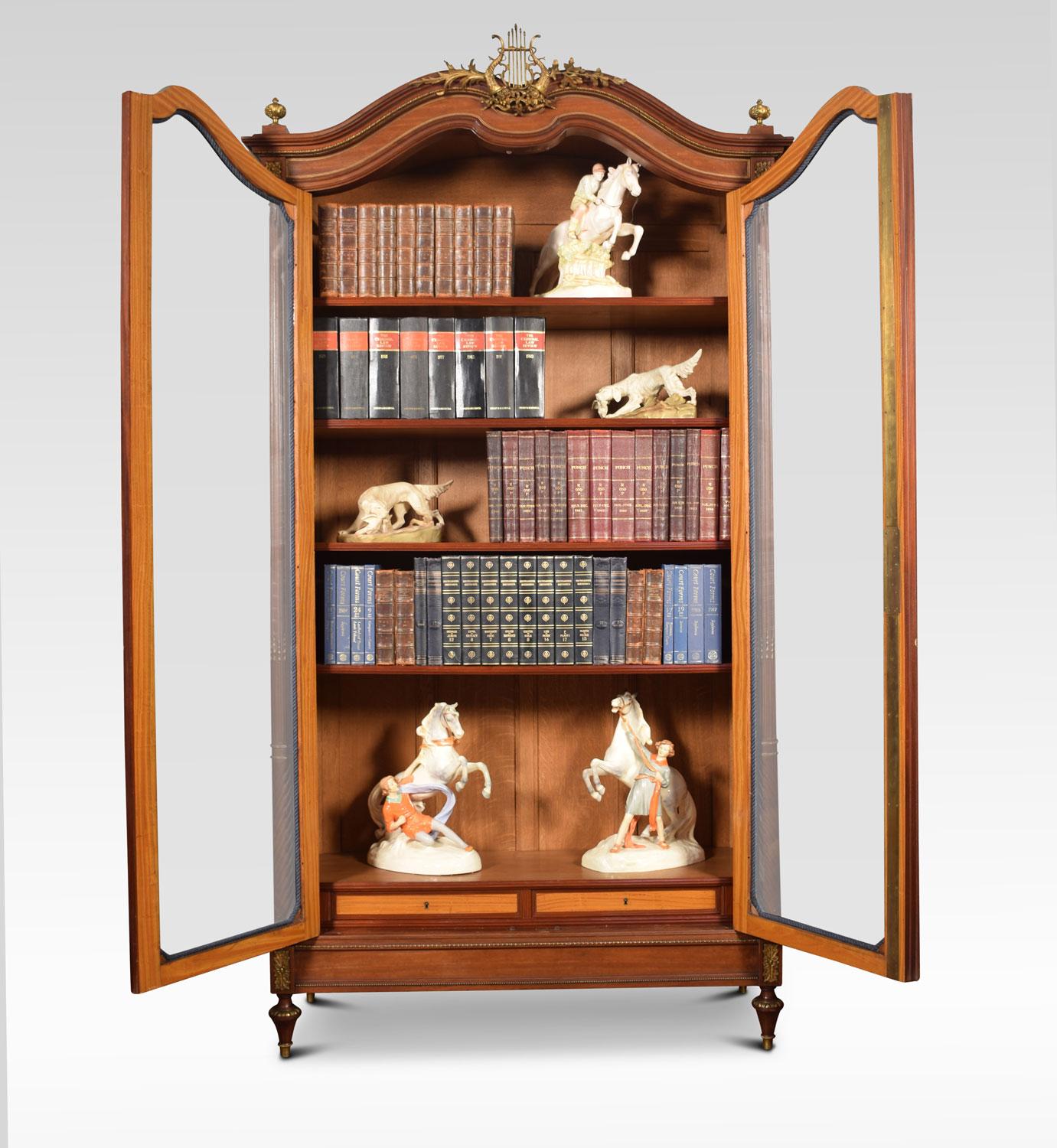Late 19th century French mahogany bookcase .The moulded cornice with central lyre motif above two large bevelled glass doors enclosing four adjustable shelves with two short draws below. All raised up on tapering brass caped feet. The bookcase will