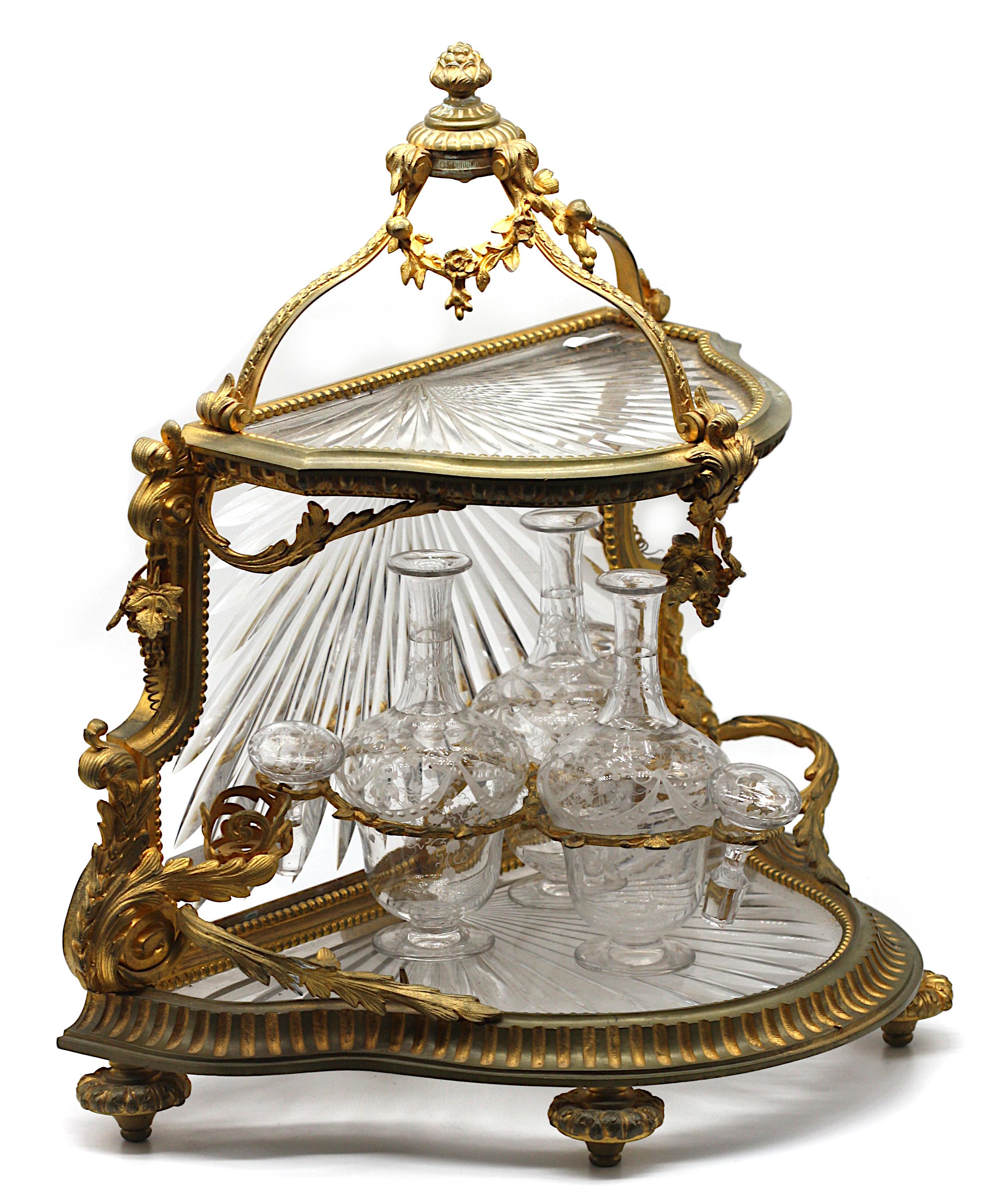 French Gilt Bronze and cut-Glass Tiered Liquor (Tantalus) Set
late 19th century, perhaps Baccarat
Of Demilune form, with an open crown, the hinged upper tier lifting up and set with a shelf cut with diagonal flutes, with a conformingly cut glass