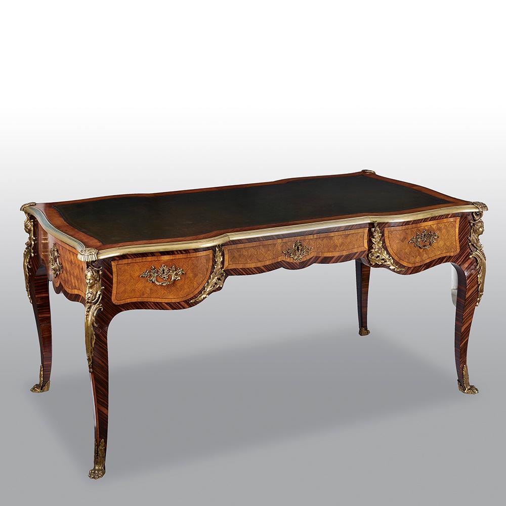 Late 19th century Kingwood and parquetry French gilt-bronze mounted bureau plat. The rectangular top with inset leather, above three fitted drawers with gilt-bronze banding, the side mounted with Bacchic masks raised on cabriole legs and terminating