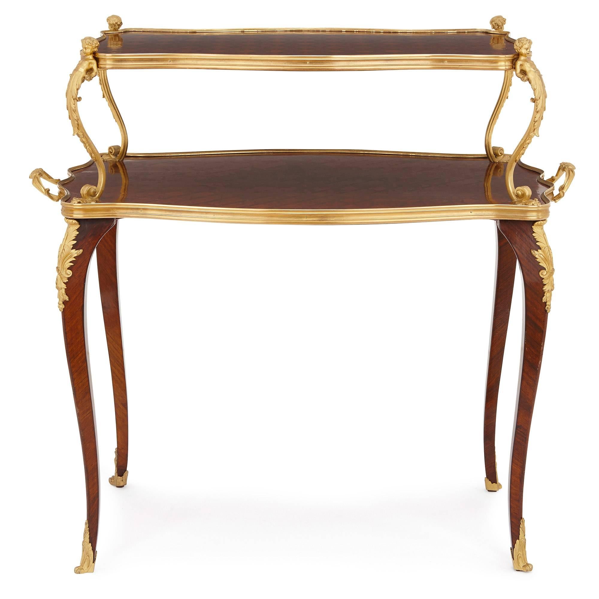 Featuring parquetry designs, exquisite curved gilt bronze mounts and a two-tier design, this beautiful tea table is the result of highly skilled craftsmanship. The upper tier of the table is topped with a diamond parquetry design, and is supported
