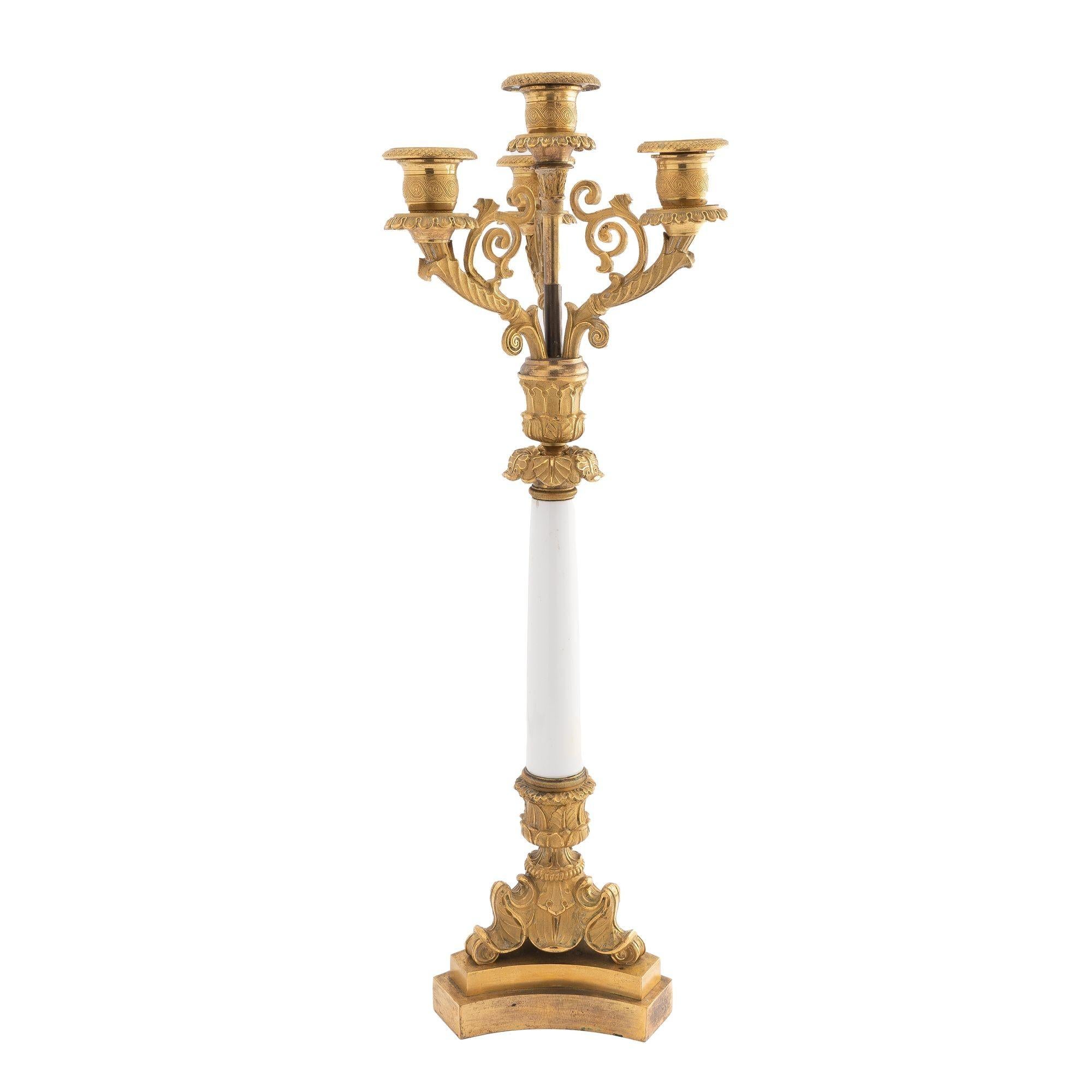 French bronze candelabra with original fire gilt finish. The candelabra has three finely cast scroll arms in the form of a cornucopia, fixed around a central shaft with a candle socket on a white opaline column mounted on a gilt bronze foliate