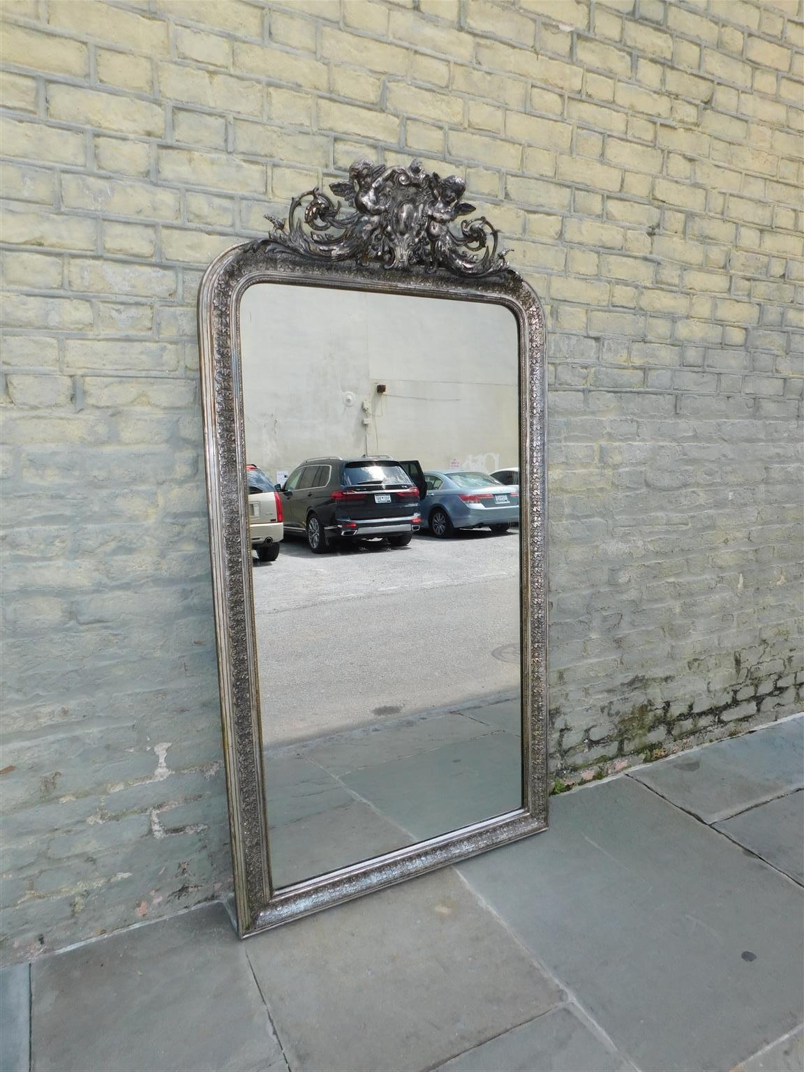 Specchio da parete francese in legno intagliato e dorato con medaglione centrale, cherubini affiancati appollaiati su decorazioni a volute intagliate ad acanto e bordo a fogliame modellato.  Lo specchio conserva il vetro originale e il supporto in