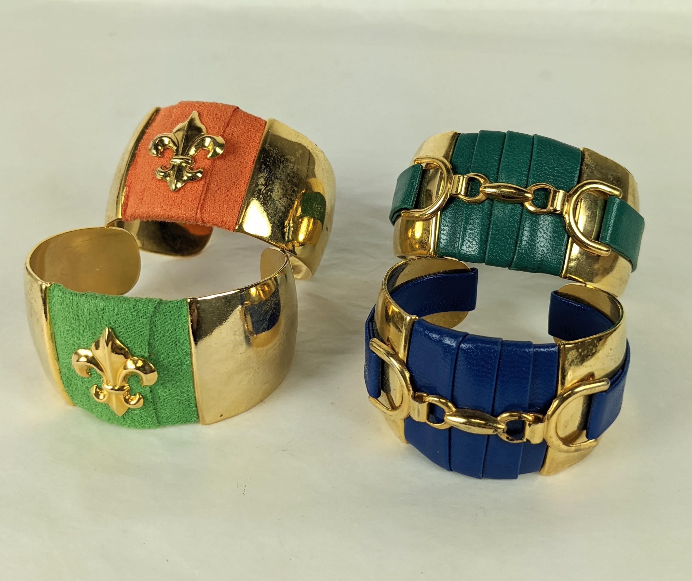 French cuff bracelets of gilt plate brass decorated with orange or green faux suede with gilt fleur de lis motifs as well as navy or forest green faux leather with horse bit motifs. Priced indiividually, please let us know which style is desired.