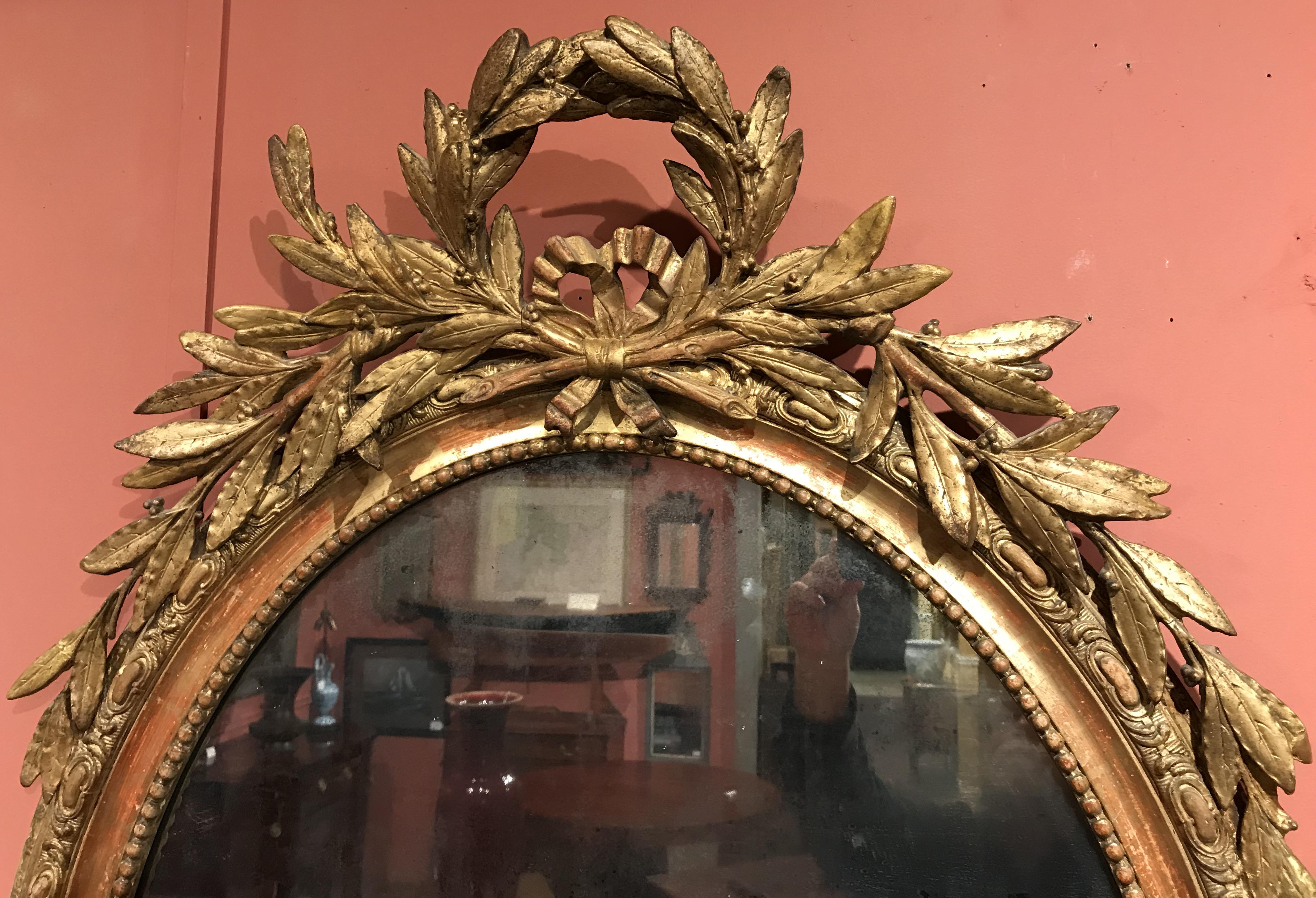A fine French gilt oval mirror with carved wooden foliate laurel decoration from the early 19th century, in very good overall condition, minor old repairs and losses, back panel stains, and other imperfections. Dimensions: 47 in H x 31 in W x 6 in D.
