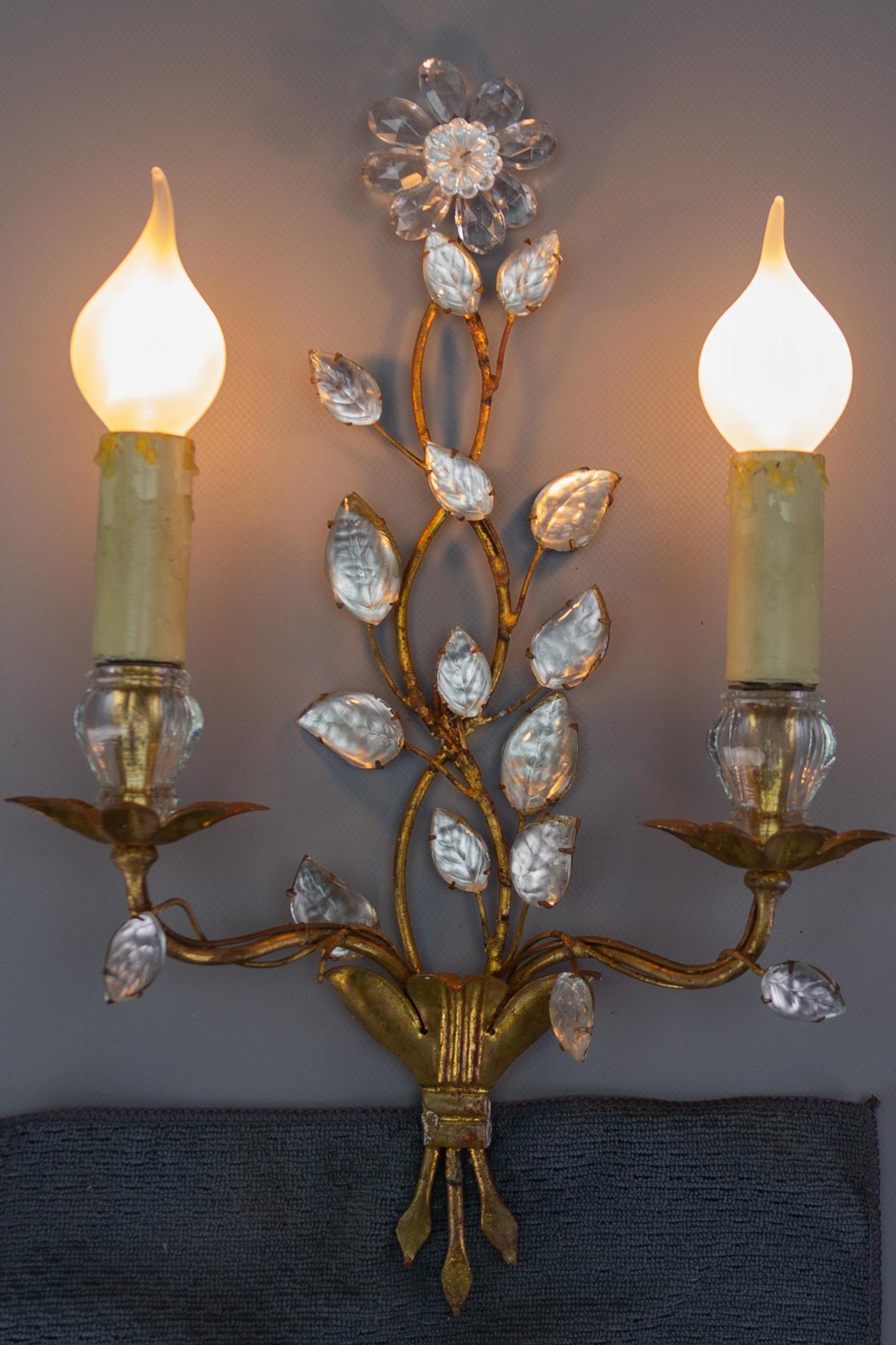 Chic and delicate French gilt metal and glass two-light wall sconce by Maison Baguès. Beautifully decorated with branches of crystal-covered leaves and a crystal flower on top. 
Two sockets for E14 size light bulbs.
Dimensions: height: 40 cm / 15.74