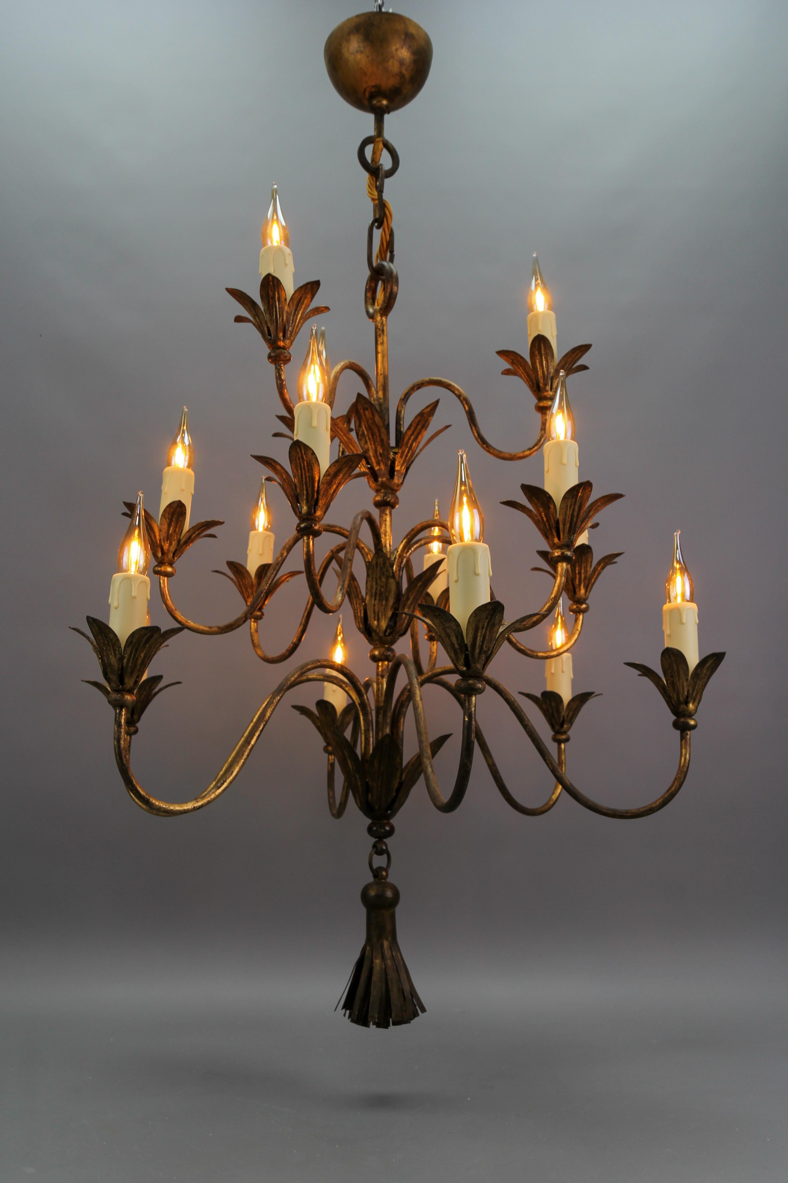 French gilt metal fifteen-light chandelier from ca. 1950s.
This impressive and rare French Hollywood Regency gilt metal chandelier features fifteen arms with flower-shaped bobeches and a gilt metal tassel in the center of the bottom of the