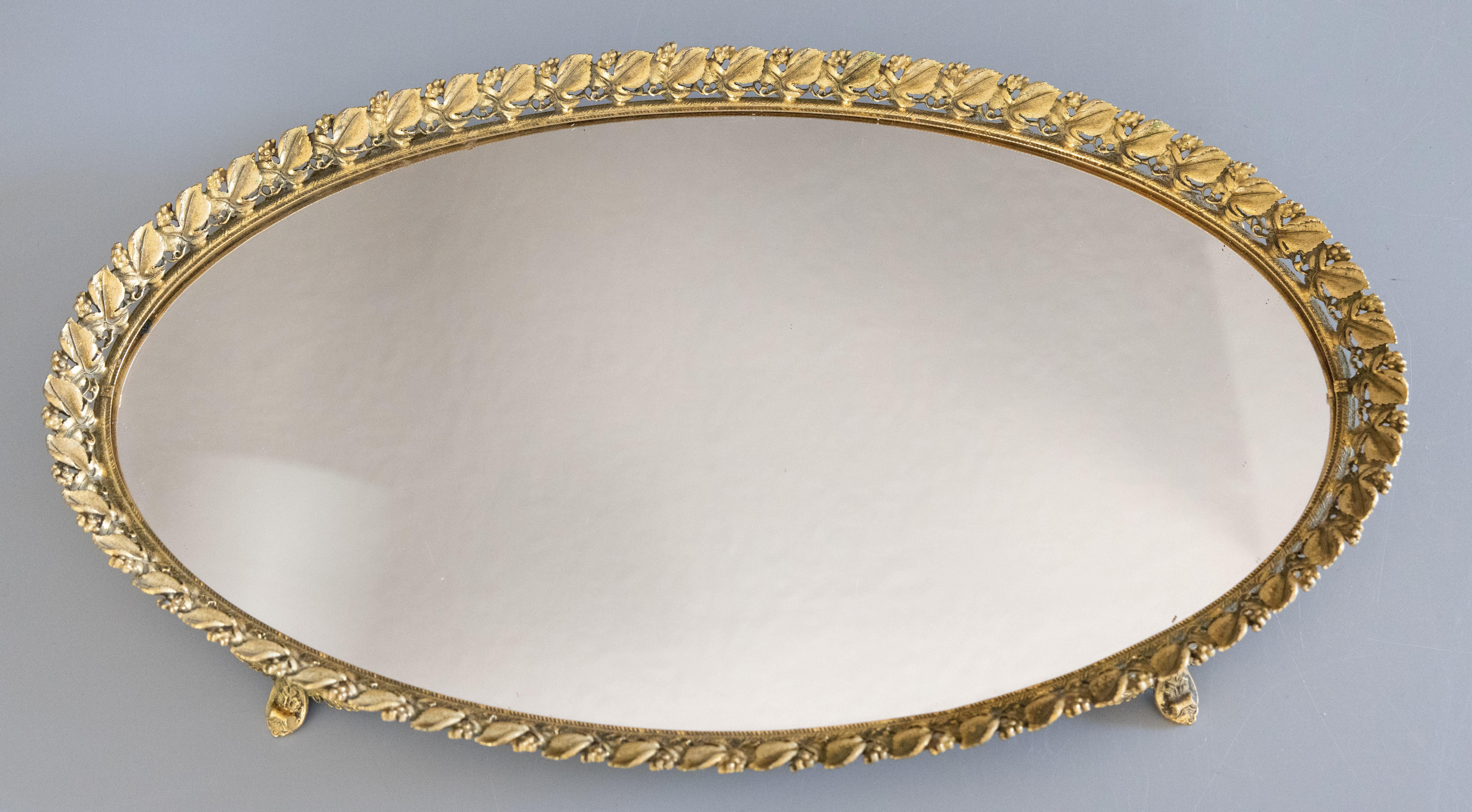 A stunning vintage French gilt ormolu oval mirror vanity or bar tray, circa 1950. This beautiful tray is a nice large oval size surrounded by a gorgeous grape leaf gallery with ornate feet in a lovely gilt patina. It would be perfect for displaying