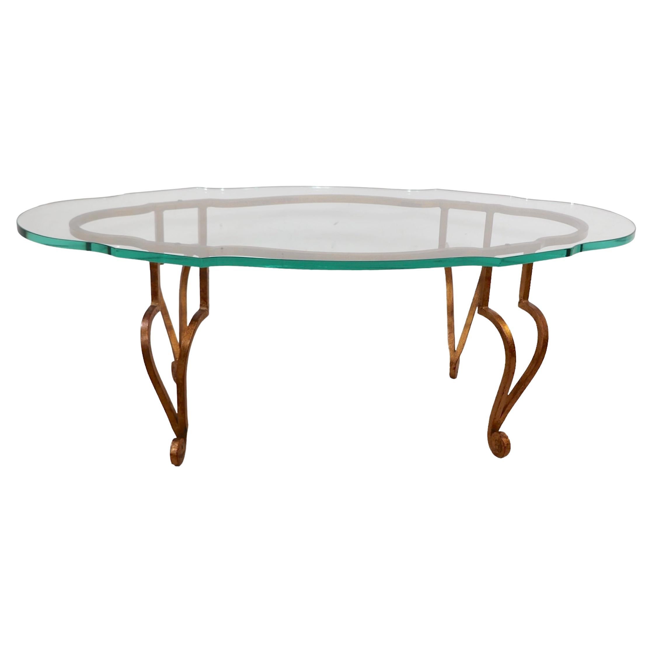 Voguistischer, schicker und stilvoller Hollywood Regency Couchtisch aus Frankreich von Maison Ramsey. Der Tisch hat eine dicke Platte aus gehärtetem Glas, die von einem Sockel aus vergoldetem Schmiedeeisen getragen wird. Dieses Exemplar befindet