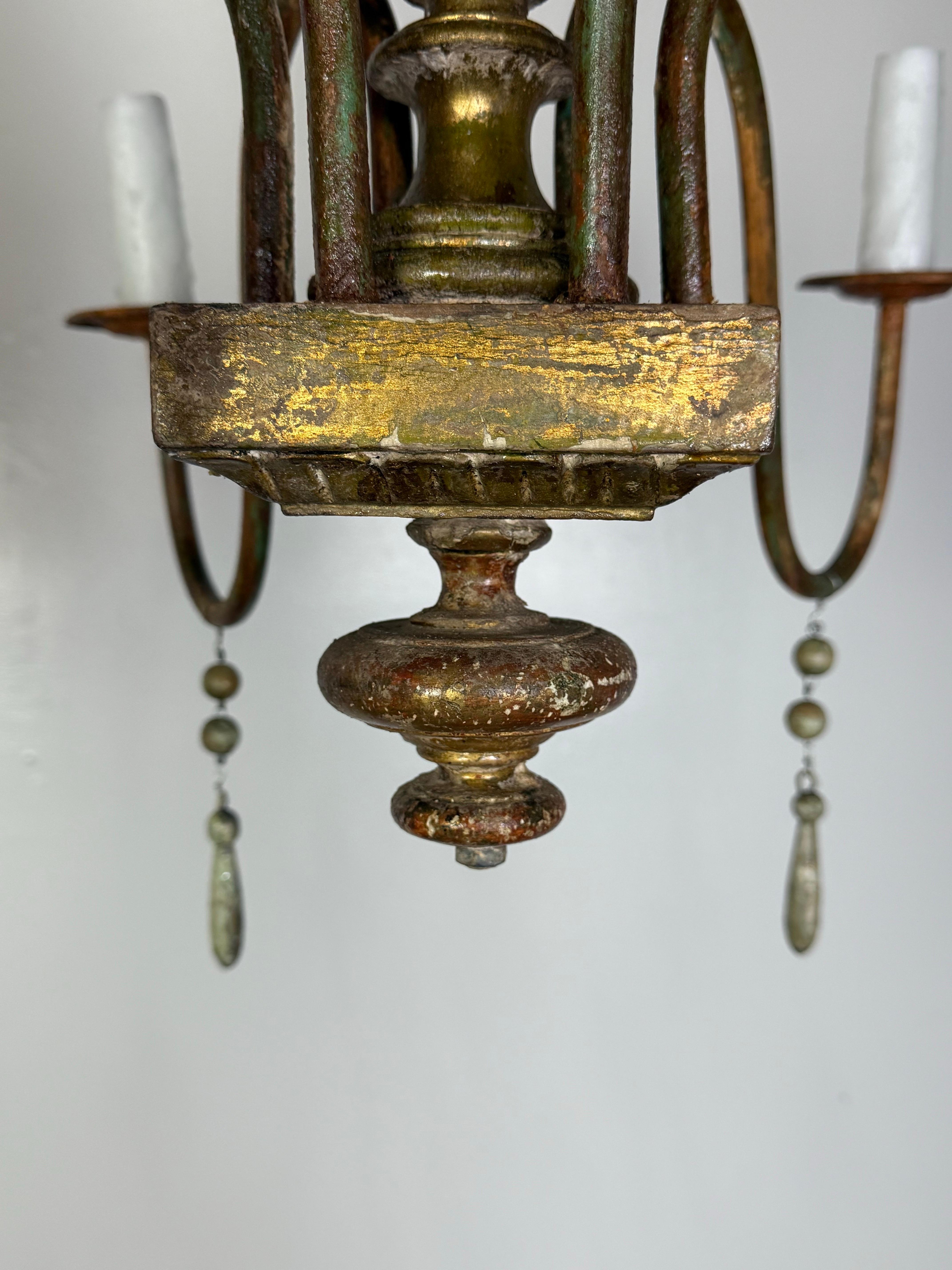 This elegant chandelier is a timeless piece with Old World charm, newly rewired for modern functionality. Featuring six gracefully curved arms in a distressed, gold gilt finish, the chandelier is anchored by a turned and fluted central column in a