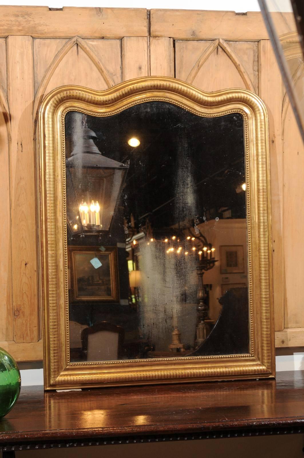 A French 19th century Louis-Philippe gold gilt mirror with rare curved top. This French Louis-Philippe mirror features a rectangular gilded frame adorned with nice patterns on the surround and surmounted with an uncommon top made of sinuous lines.