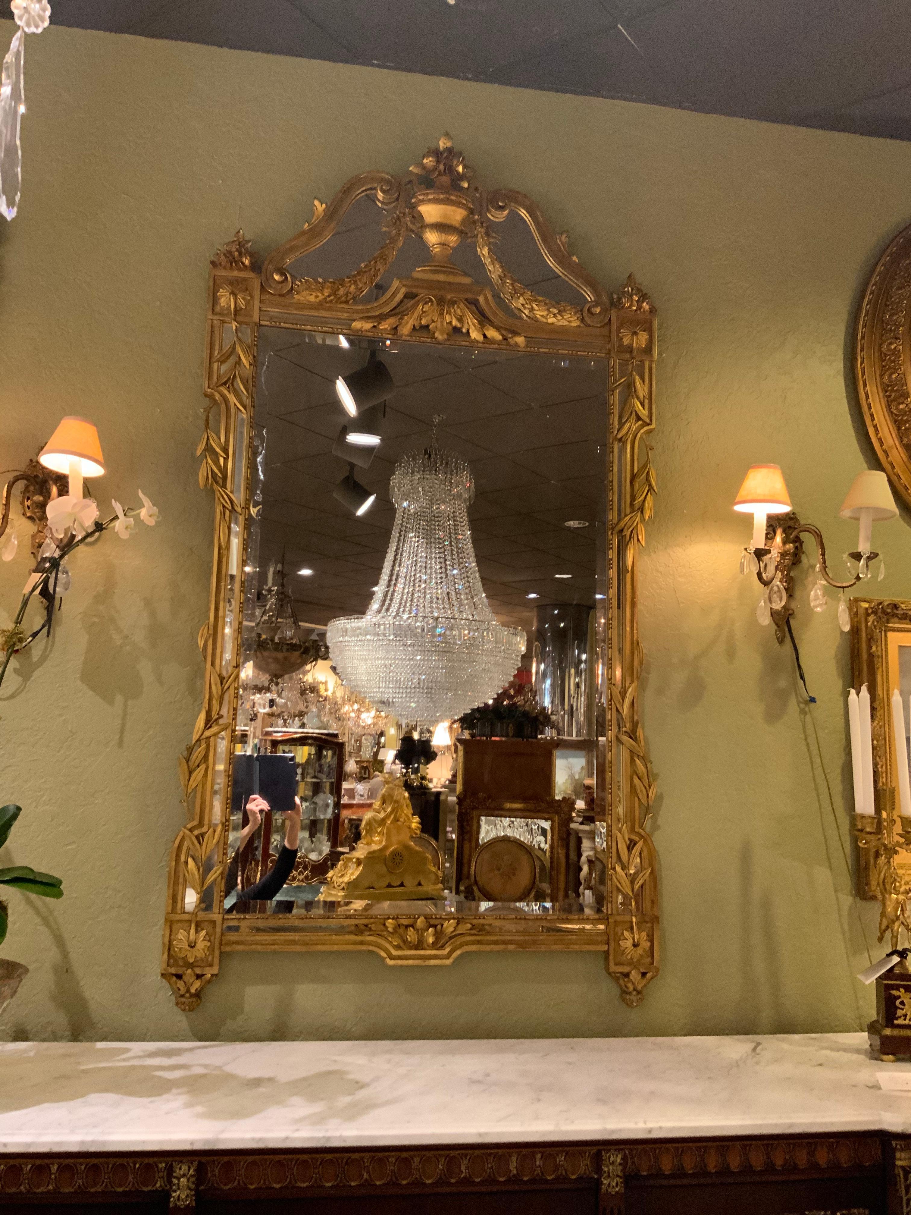 Giltwood mirror with original gilding having a leaf design on each side trailing
Vertically. A large urn is centered at the top with a floral motif at the top crest.