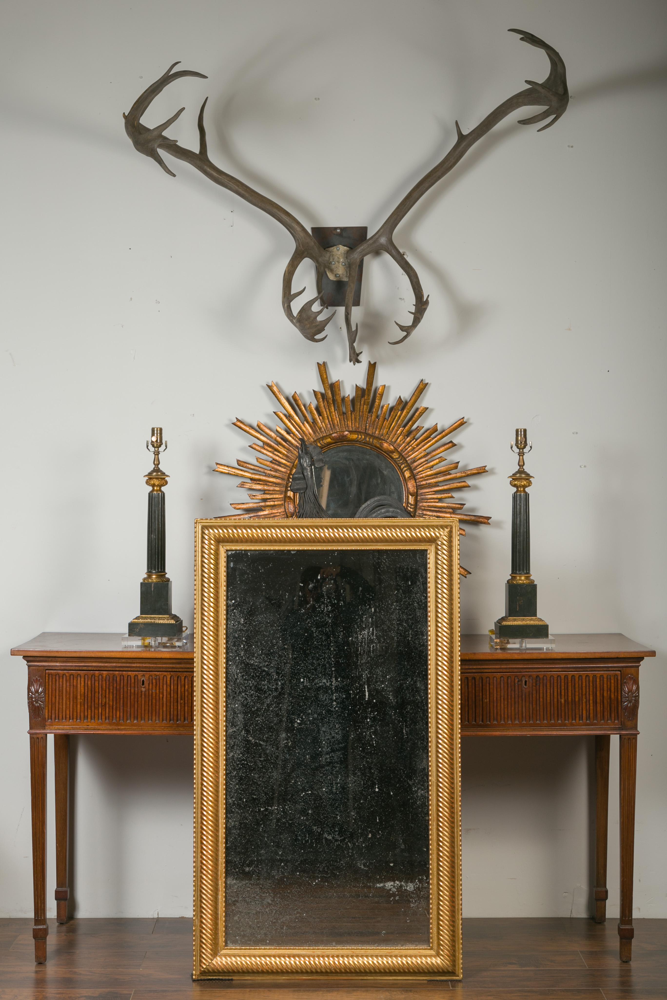 A French giltwood rectangular mirror from the early 20th century, with twisted motifs. Created in France during the turn of the century, this tall rectangular mirror captures our attention with its golden finish accented with red undertones,