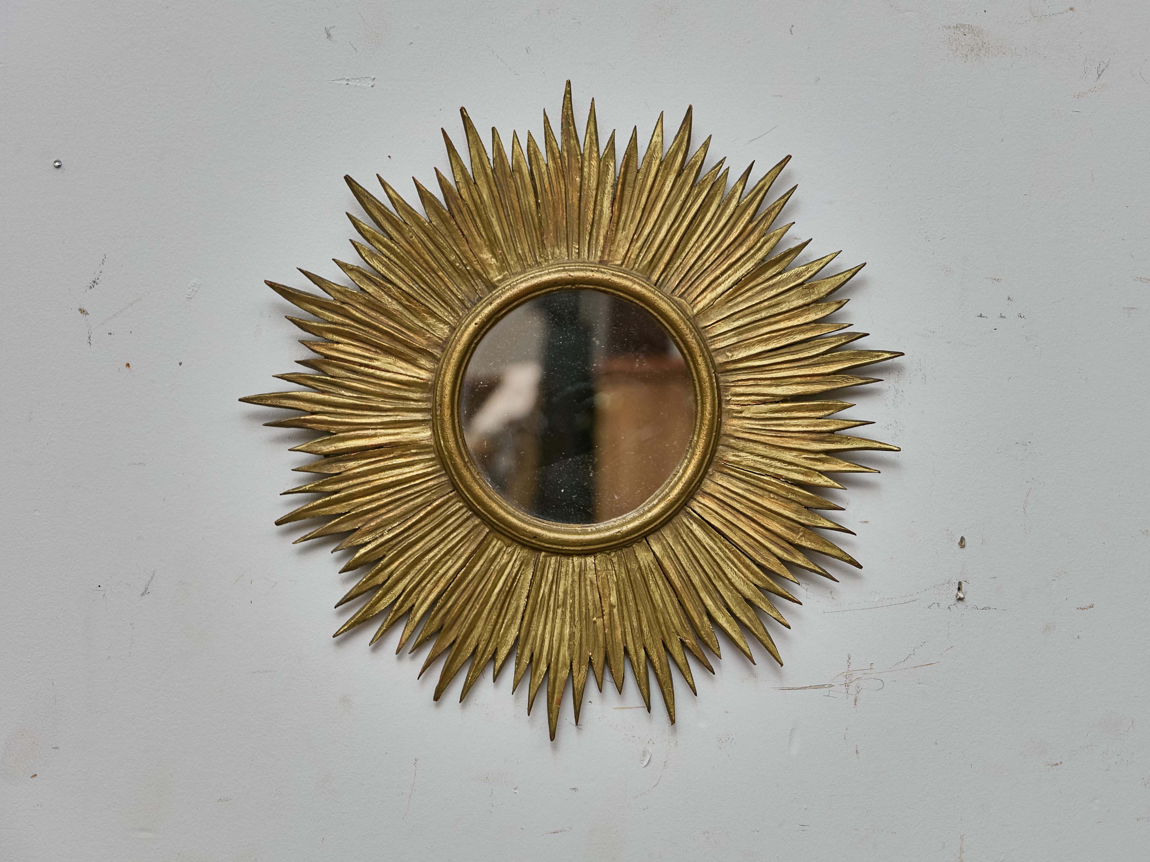Un sorprendente specchio francese a raggiera degli anni '30-'40, realizzato in legno intagliato e rifinito con una calda doratura. Con un diametro di circa 18 pollici, questo specchio da parete decorativo presenta una disposizione drammatica di